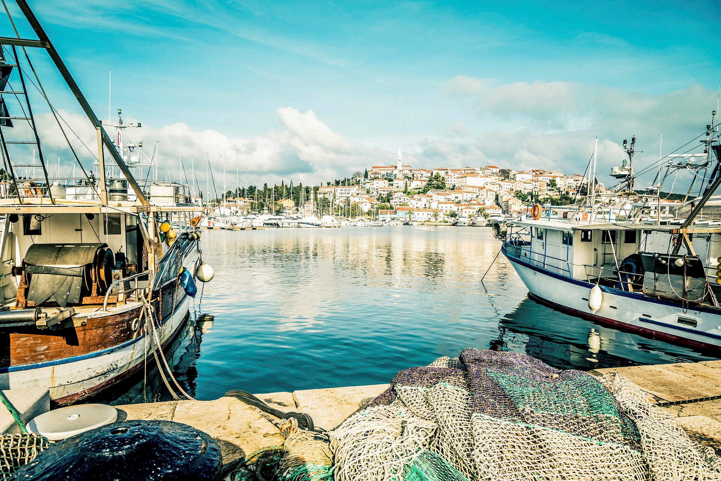 En småbåtshamn med fiskebåtar vid kajen, och en stad med små hus i bakgrunden. (AI-genererad text)