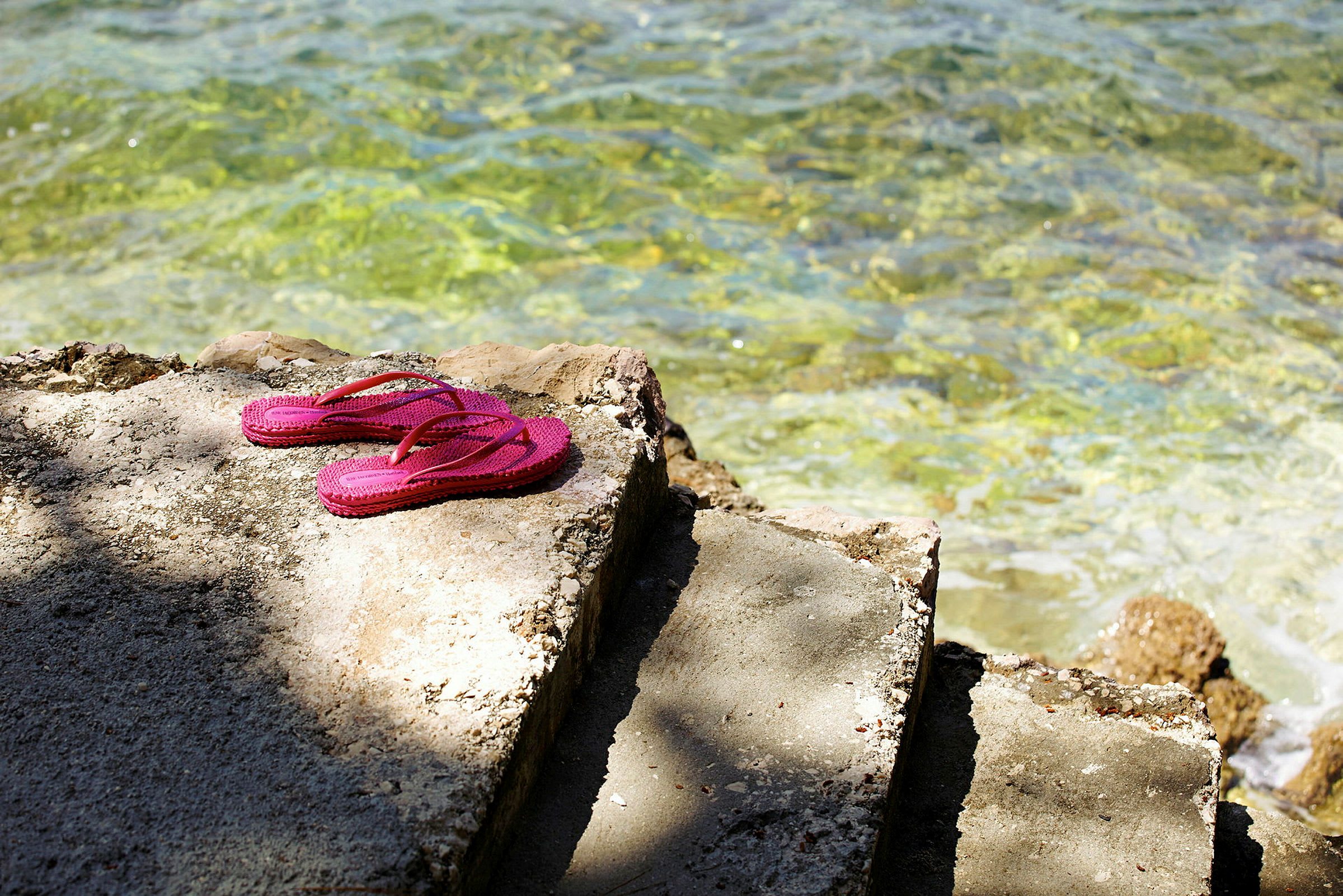 Rosa flipflops ligger på en cementtrappa vid klart vatten. (AI-genererad text)