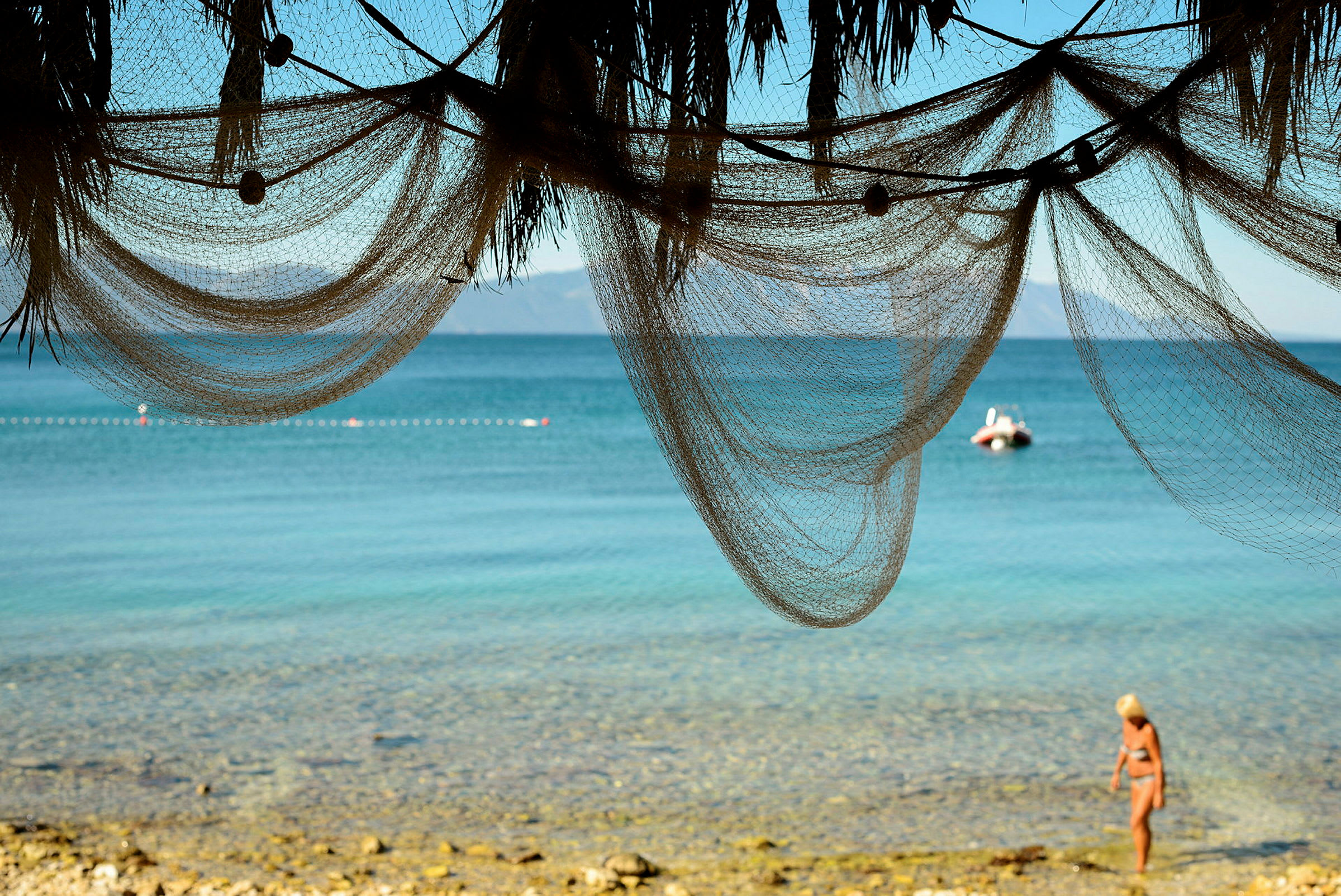 Utsikt över havet från stranden med en person som går nära vattnet under hängande nät. (AI-genererad text)