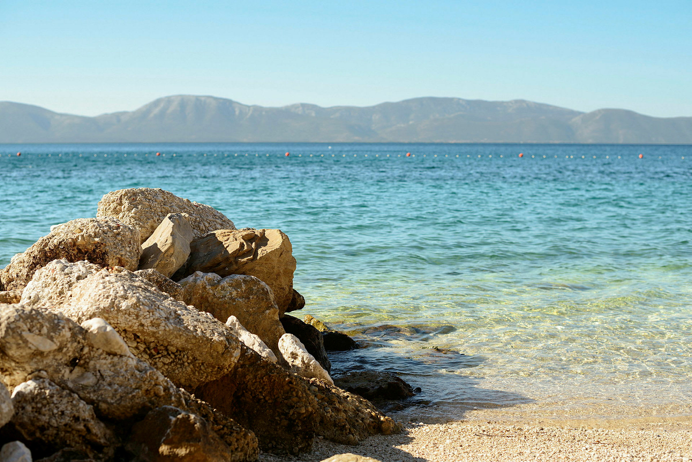 Strand med vatten och stenar i förgrunden, berg i bakgrunden. (AI-genererad text)