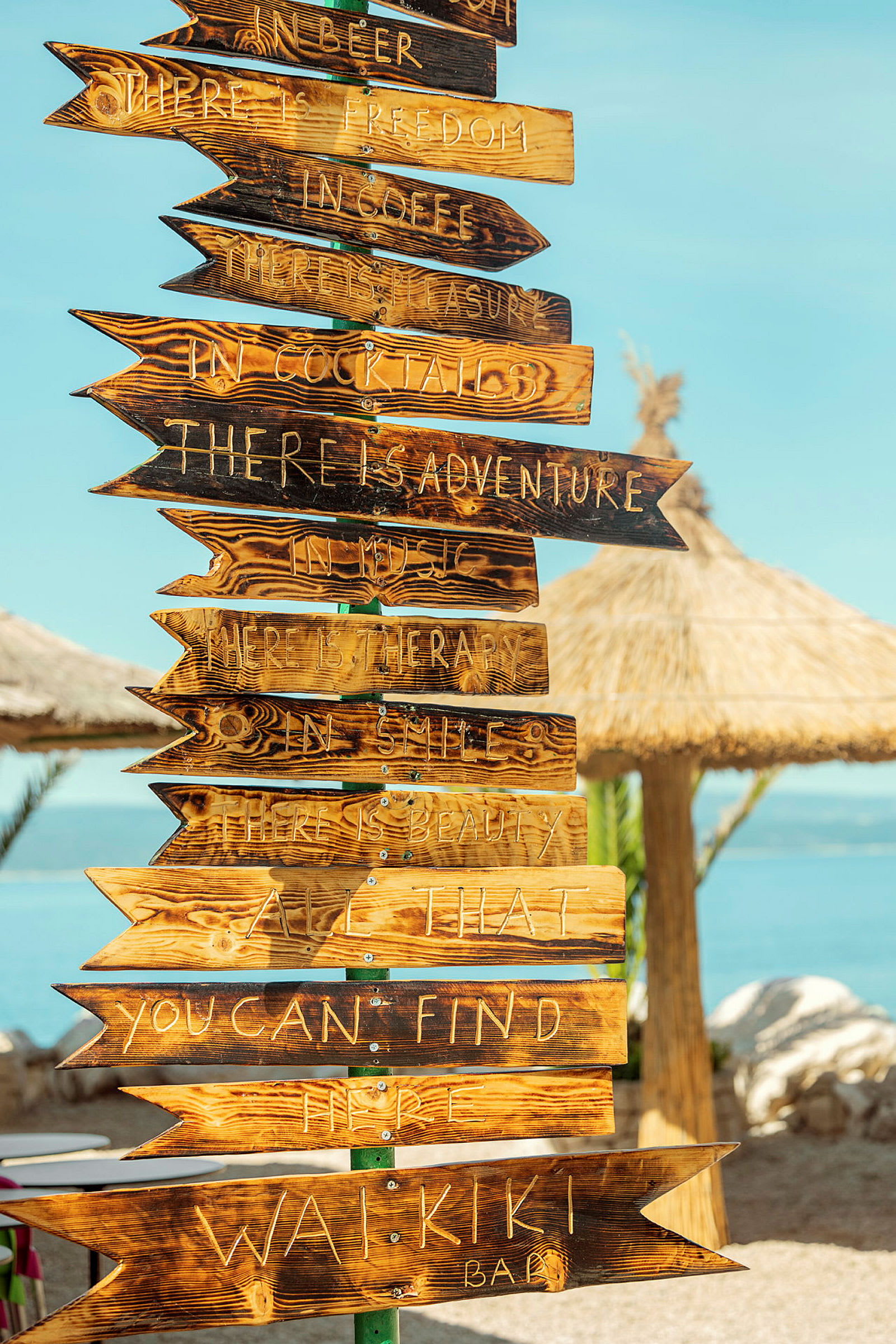 Träpilar med ingraverad text som fungerar som skyltar vid en strandbar. (AI-genererad text)