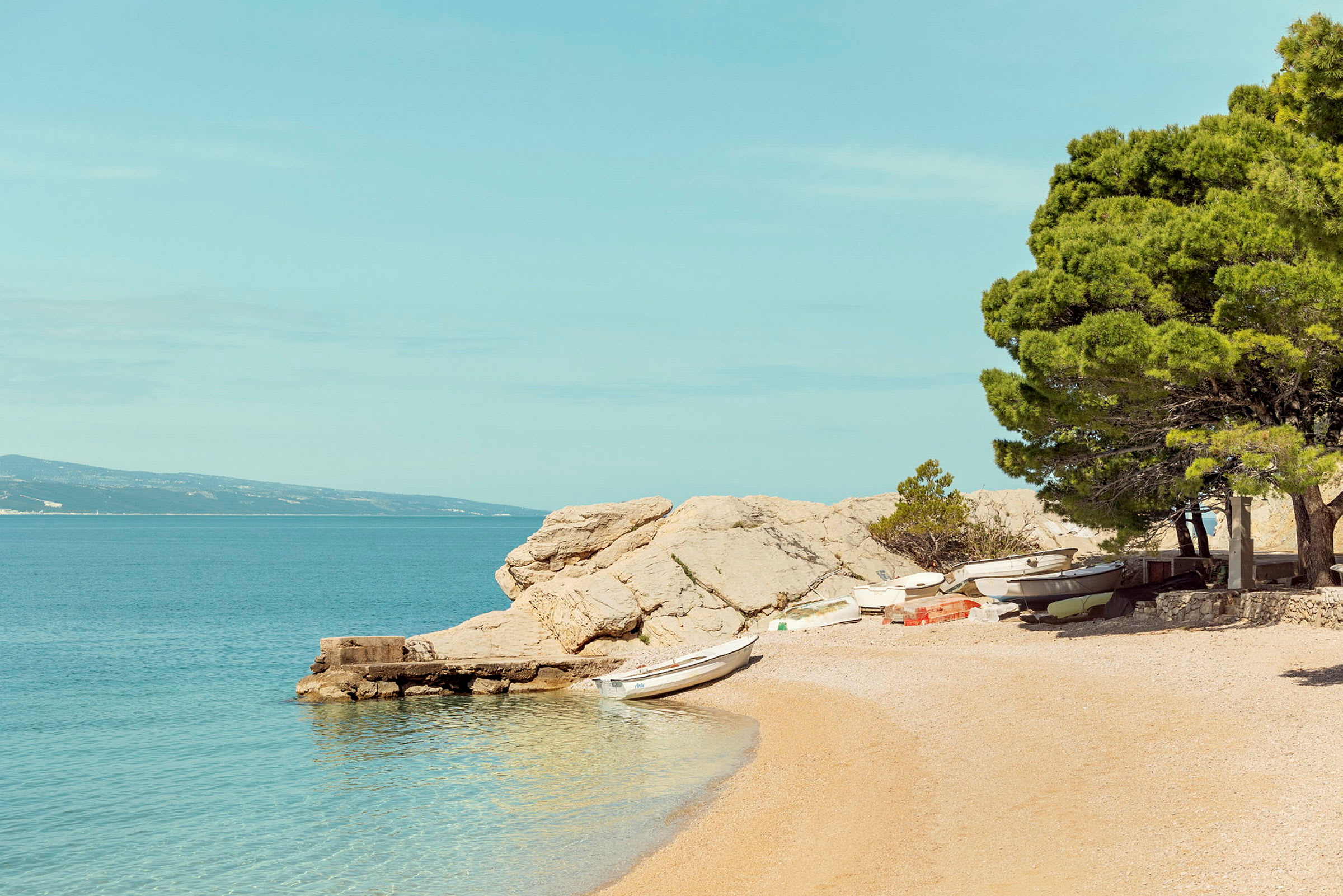 En strand med småbåtar, träd och klippor vid vattnet. (AI-genererad text)