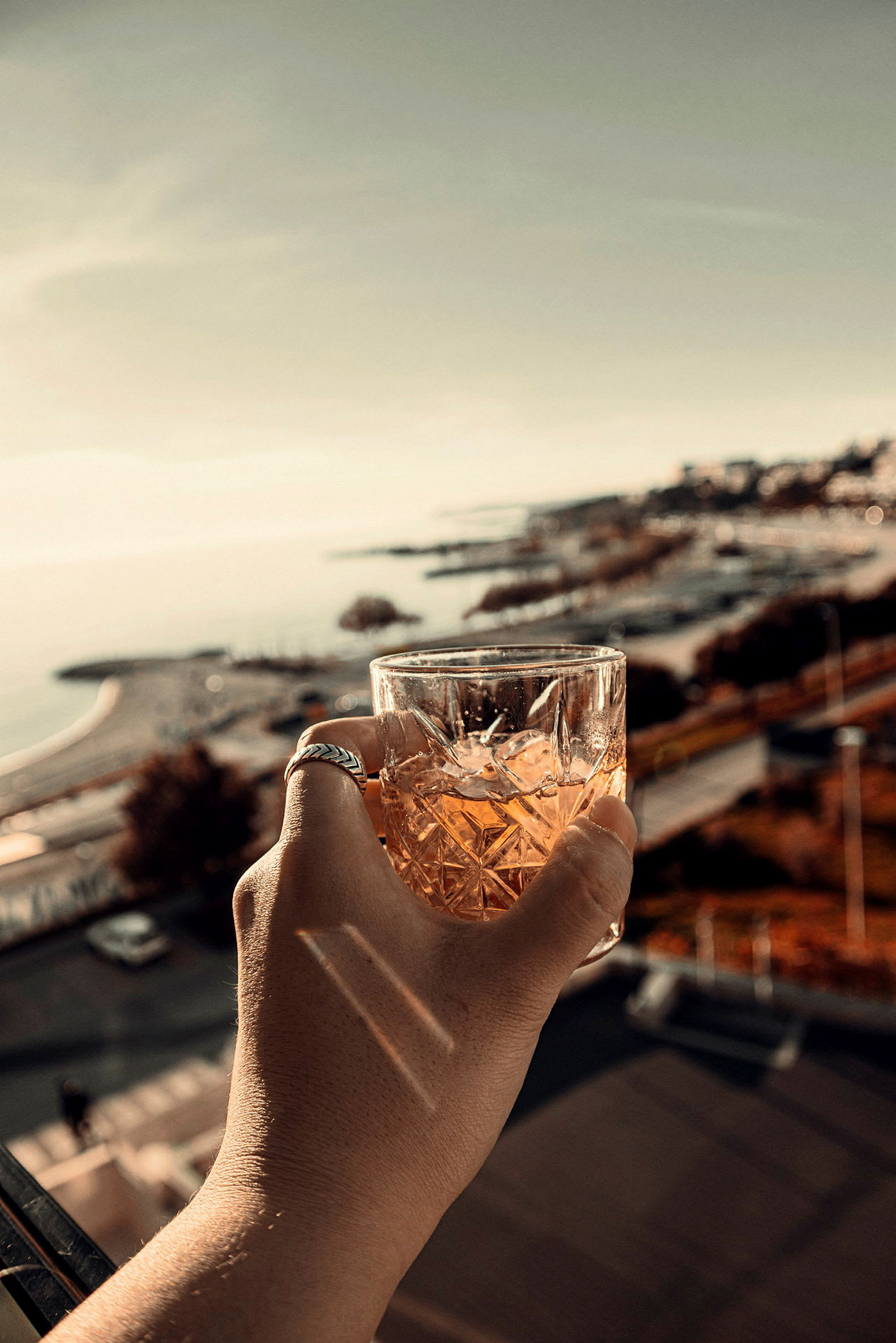 En hand håller ett glas med dryck framför en kustutsikt. (AI-genererad text)