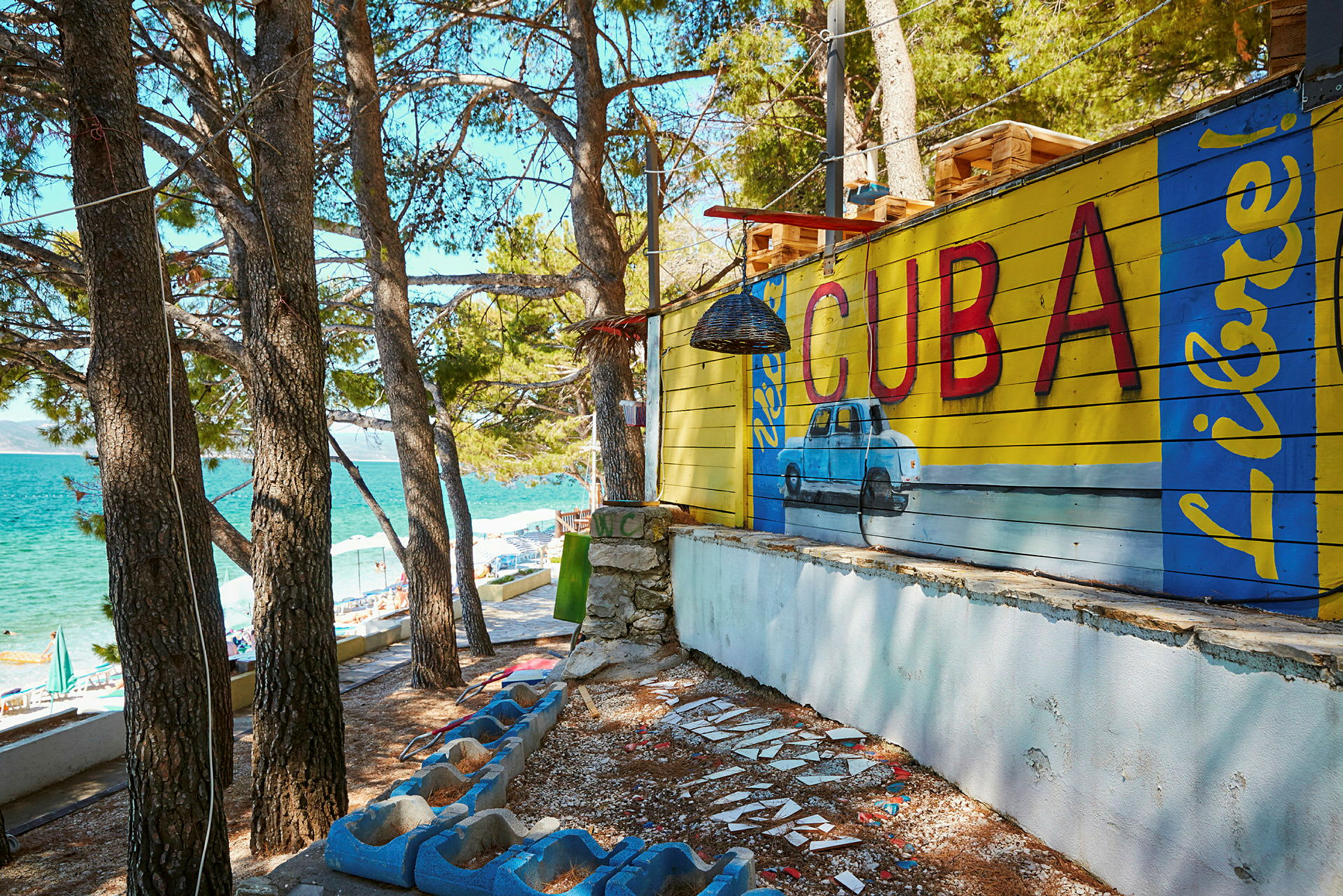 Väggmålning med texten 'Cuba' och en blå bil i tropisk miljö. (AI-genererad text)