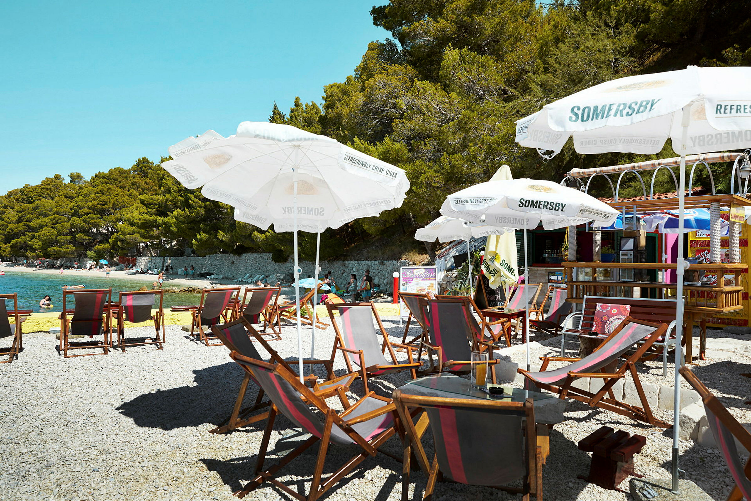 Strand med solsängar, parasoller och ett café i bakgrunden. (AI-genererad text)