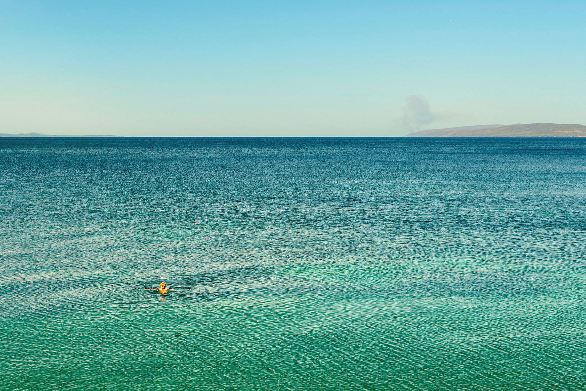 Person simmar i havet under blå himmel. (AI-genererad text)