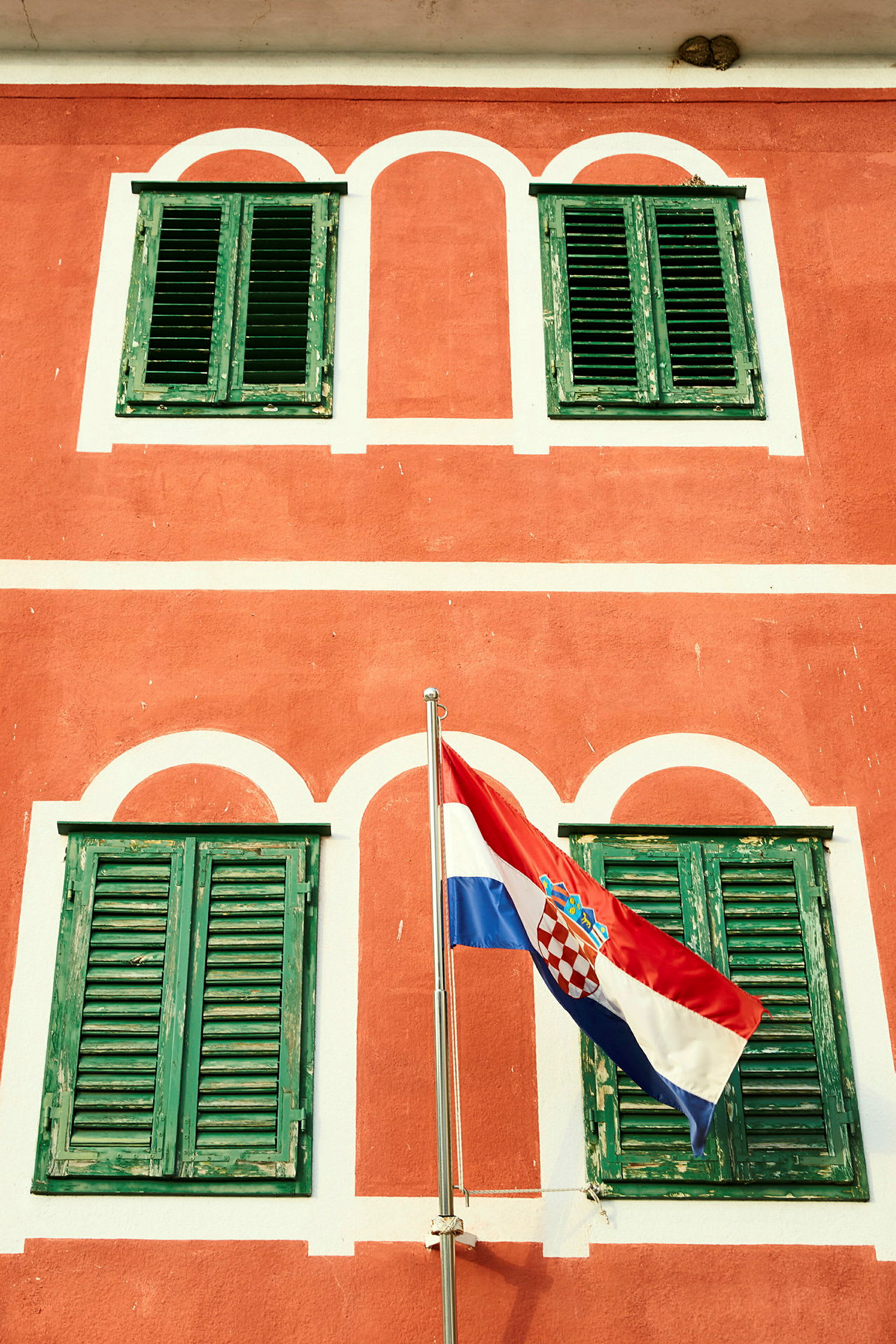 En röd byggnad med gröna fönsterluckor och Kroatiens flagga framför. (AI-genererad text)