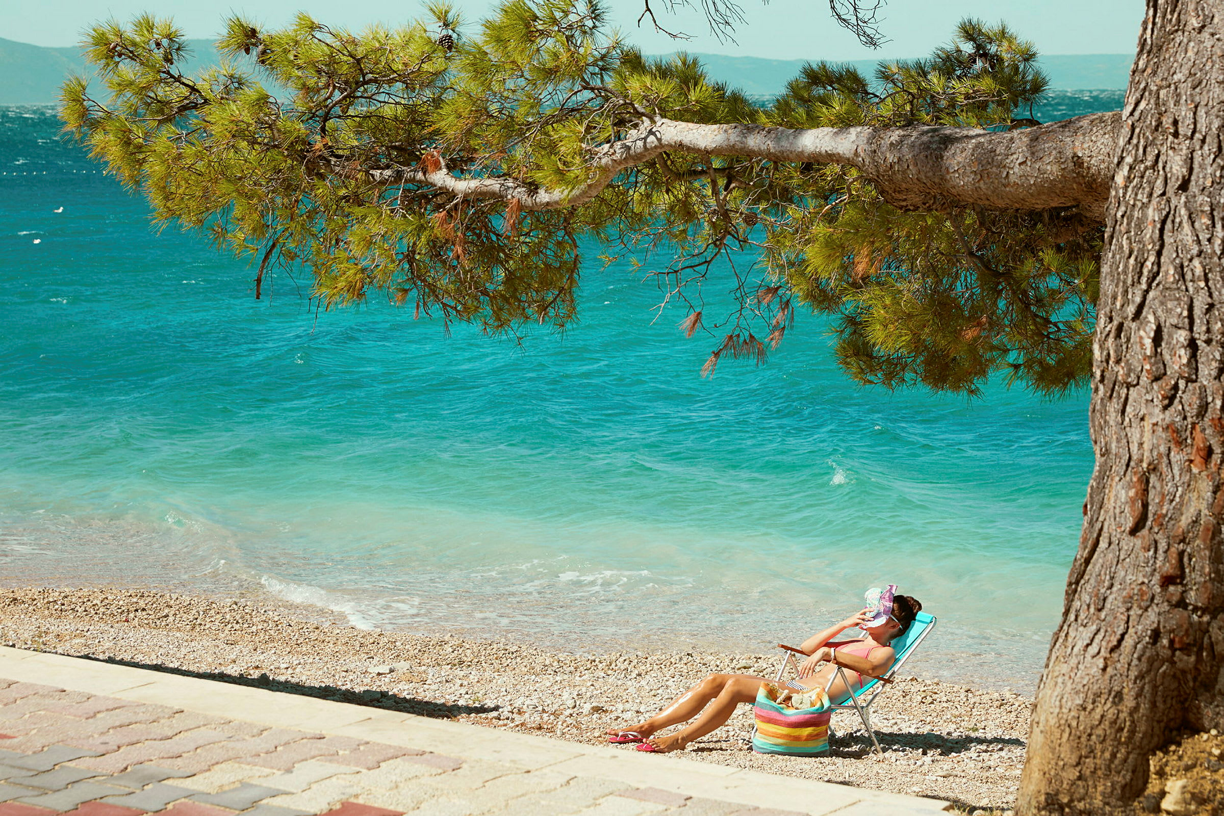 En person sitter i en solstol på en stenstrand med havet i bakgrunden. (AI-genererad text)