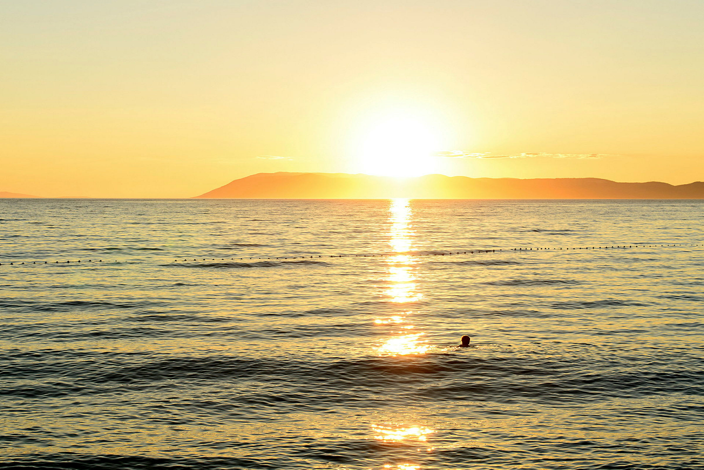 Solnedgång över havet med en siluett av en simmande person. (AI-genererad text)