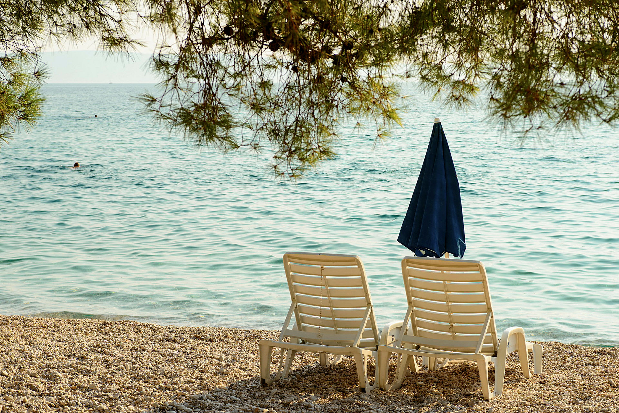 Två solstolar och ett parasoll vid en stenstrand med havet i bakgrunden. (AI-genererad text)