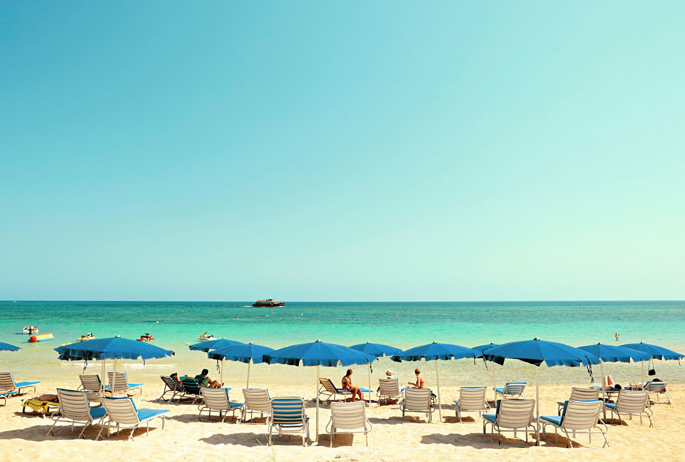 Strand med parasoller, solsängar och personer vid vattenkanten. (AI-genererad text)