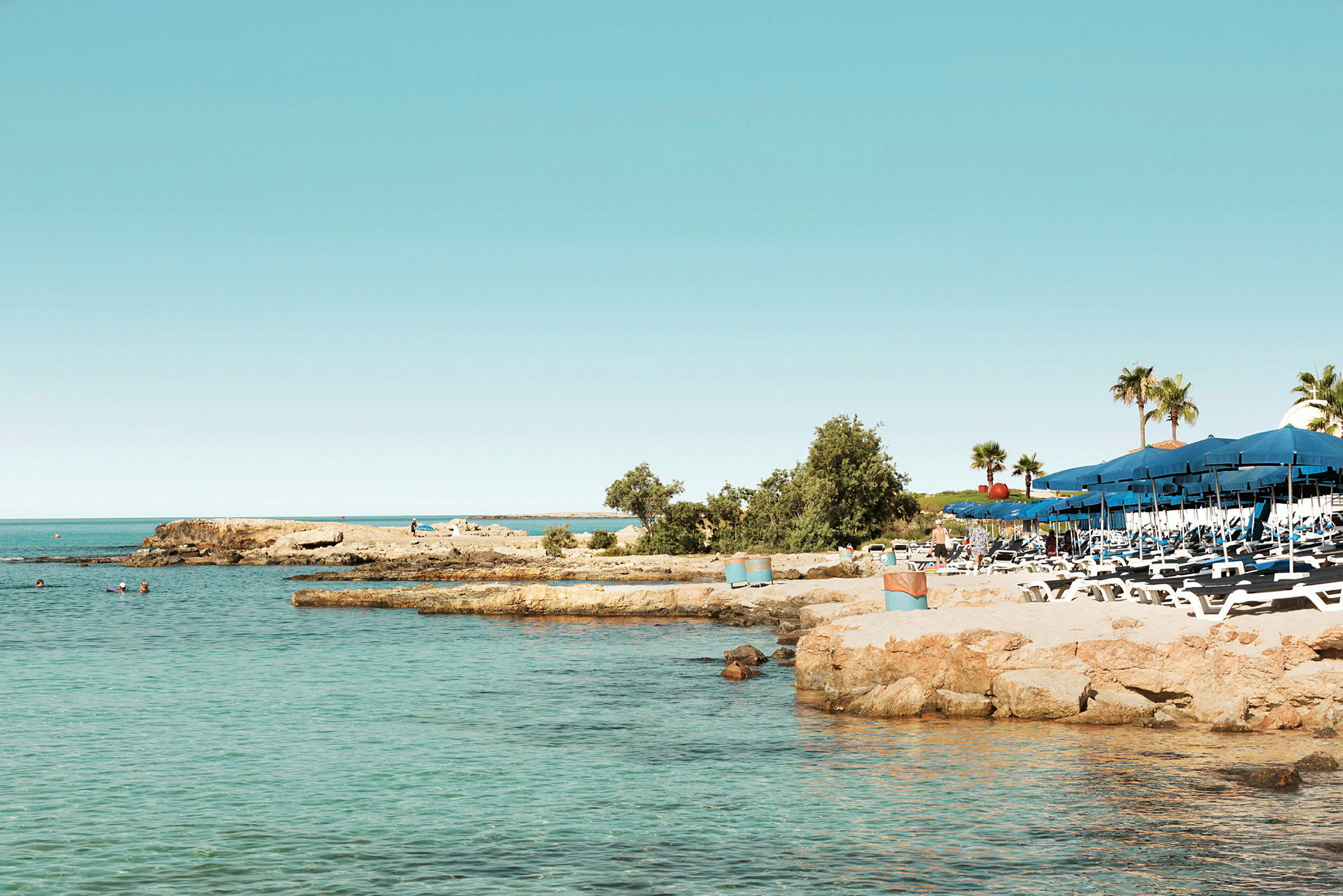 Bild av en strand med solstolar och parasoller bredvid klart vatten. (AI-genererad text)