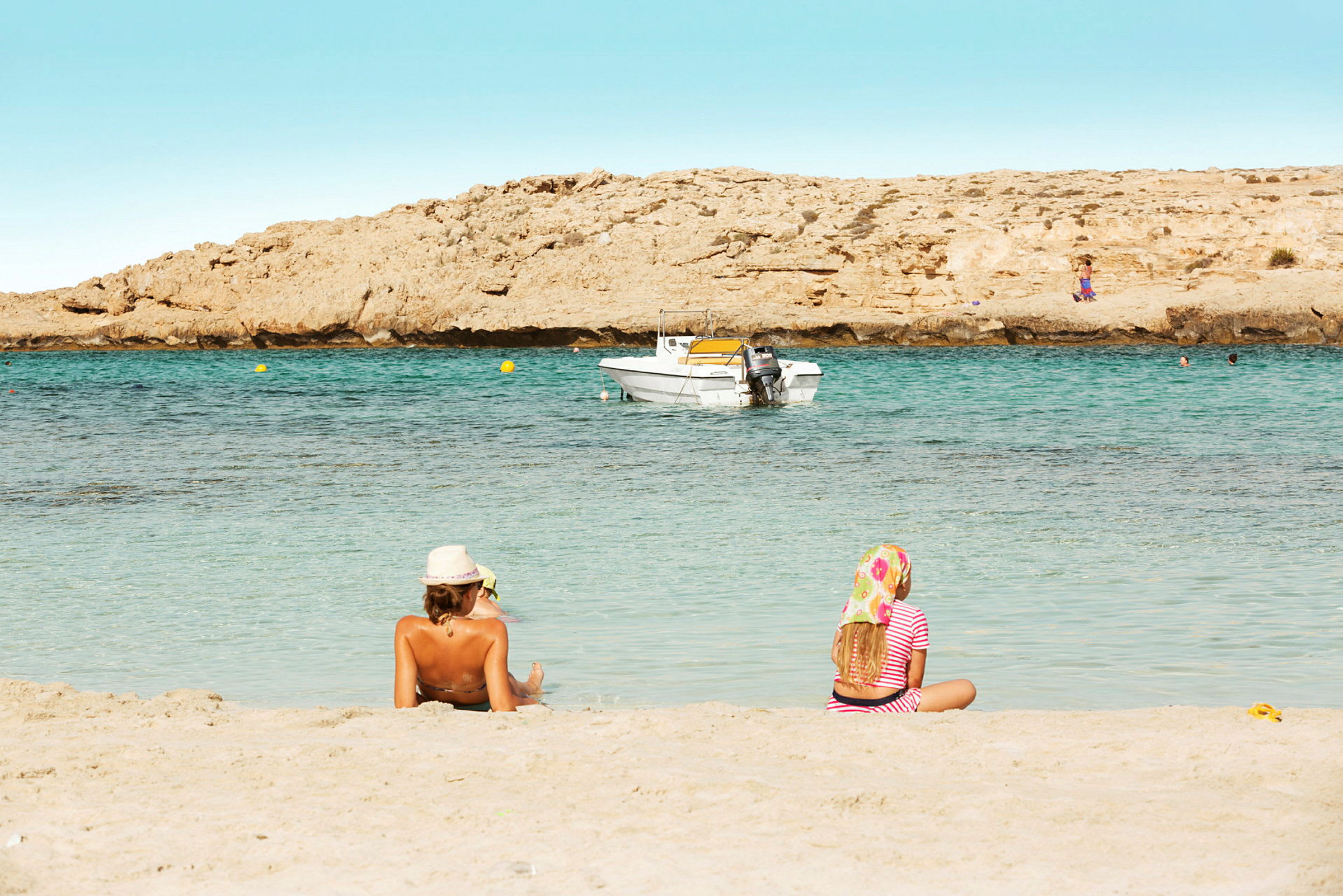Två personer sitter på en sandstrand med havet och en båt i bakgrunden. (AI-genererad text)