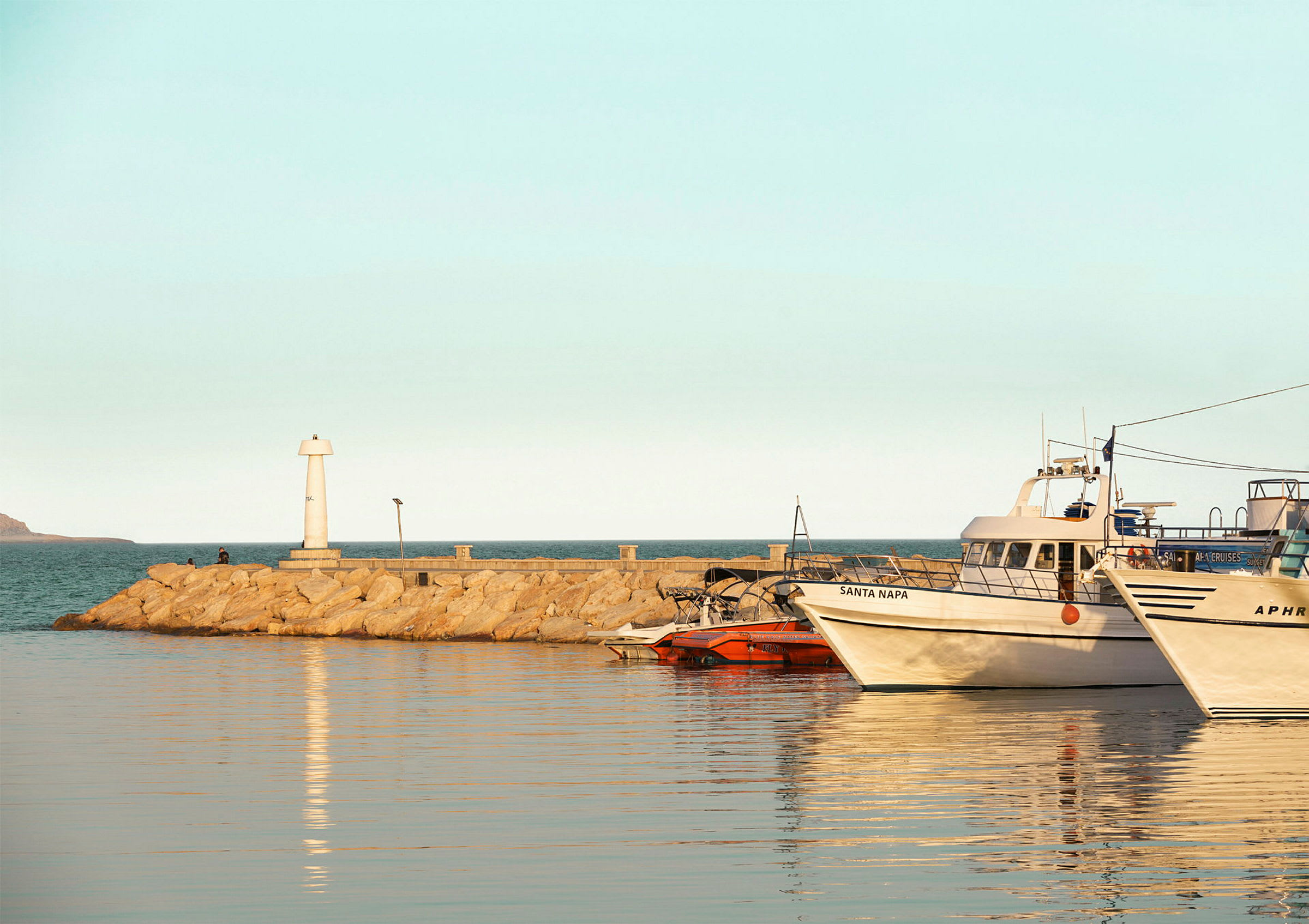 En hamn med båtar förtöjda, en fyr på en stenbrygga och lugnt vatten. (AI-genererad text)