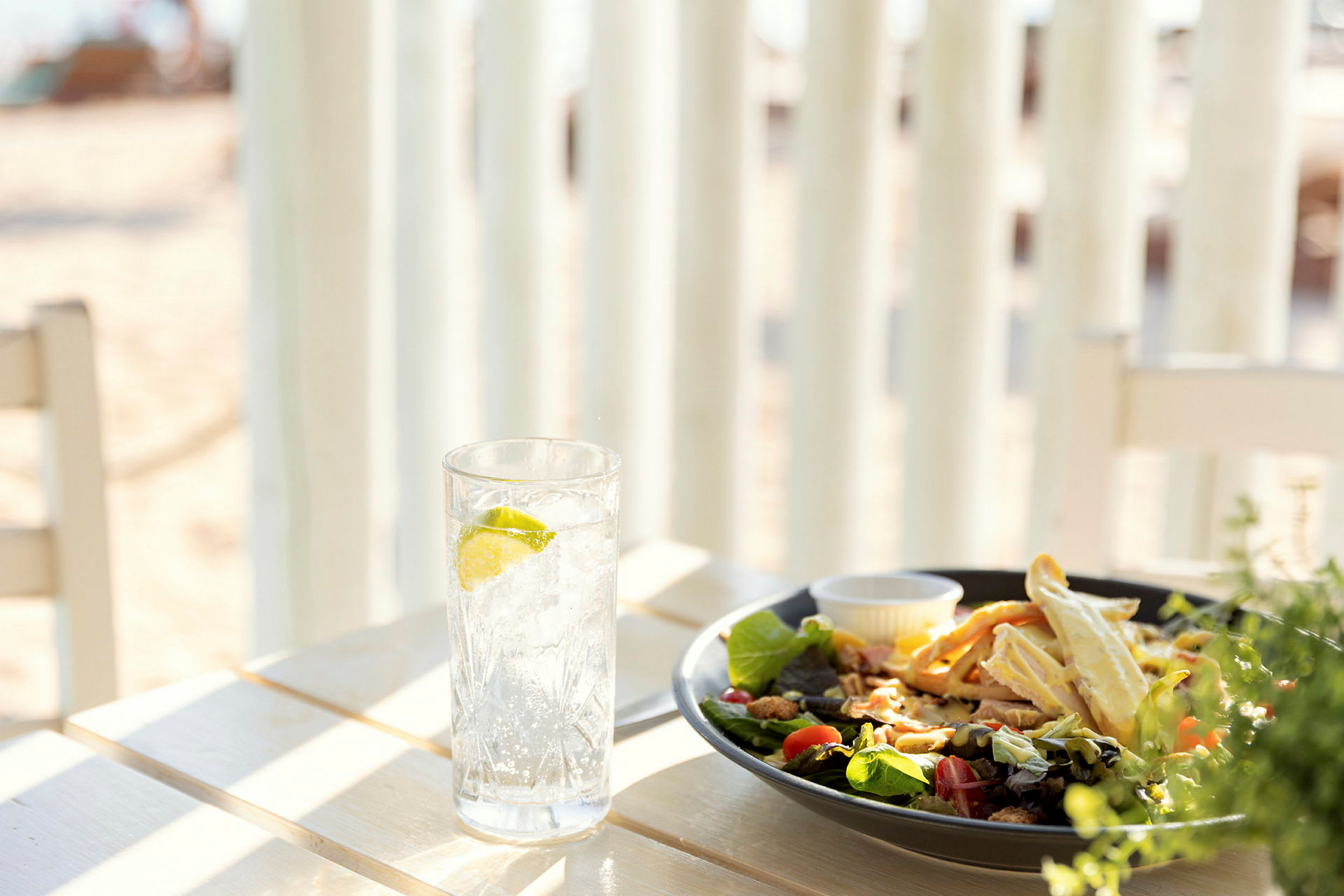 Ett bord med ett glas vatten med lime och en tallrik sallad vid stranden. (AI-genererad text)