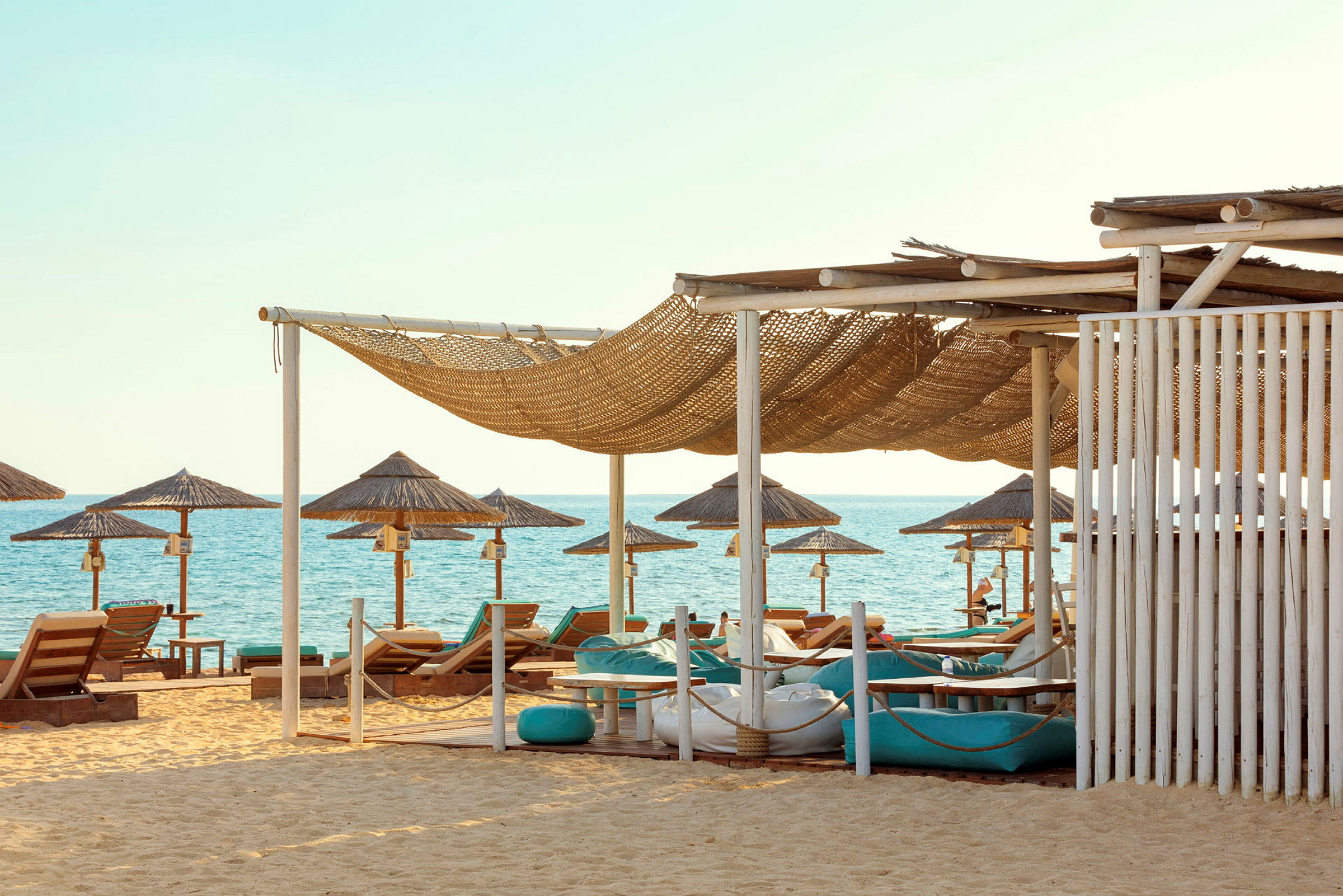 Bild av en strand med solstolar, parasoller och skuggande tak vid havet. (AI-genererad text)