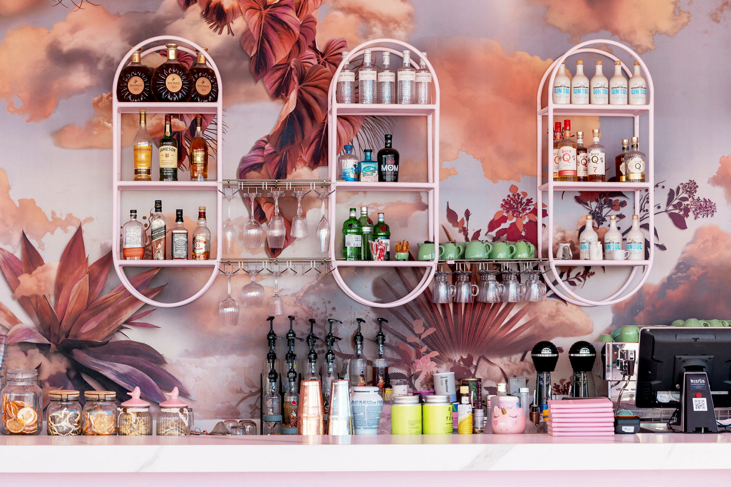 En bar med rosa hyllor fyllda med spritflaskor, glas och kaffegrönskande dekor. (AI-genererad text)