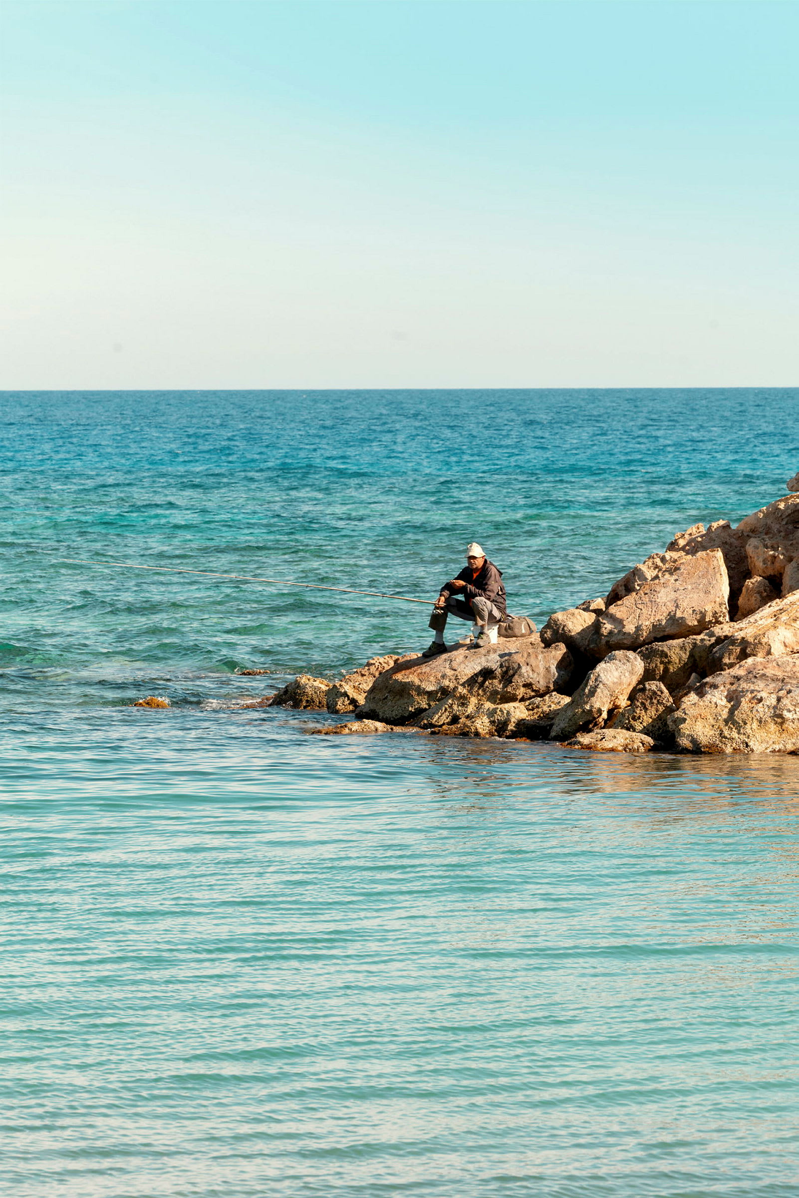 En strand med klippor vid havet, med en person som håller fiskespö. (AI-genererad text)
