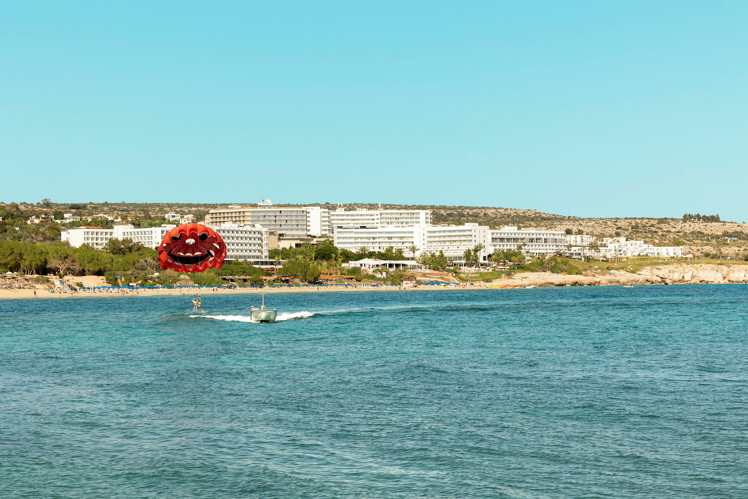 Bild av en strand med ett hotell i bakgrunden och en person som parasailer framför. (AI-genererad text)