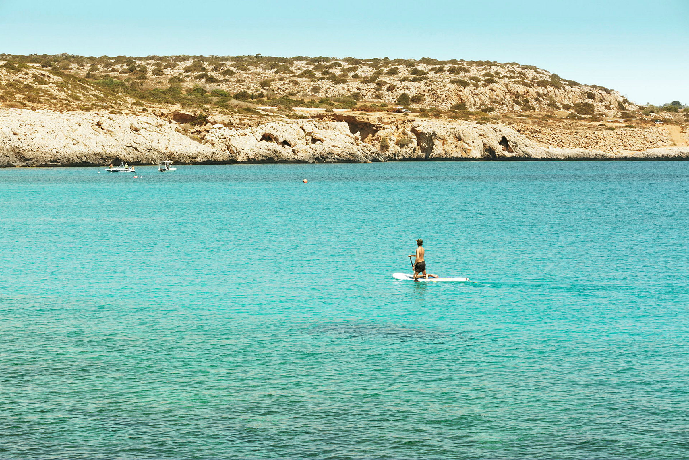 En människa som paddlar på en paddleboard med klippor och hav i bakgrunden. (AI-genererad text)