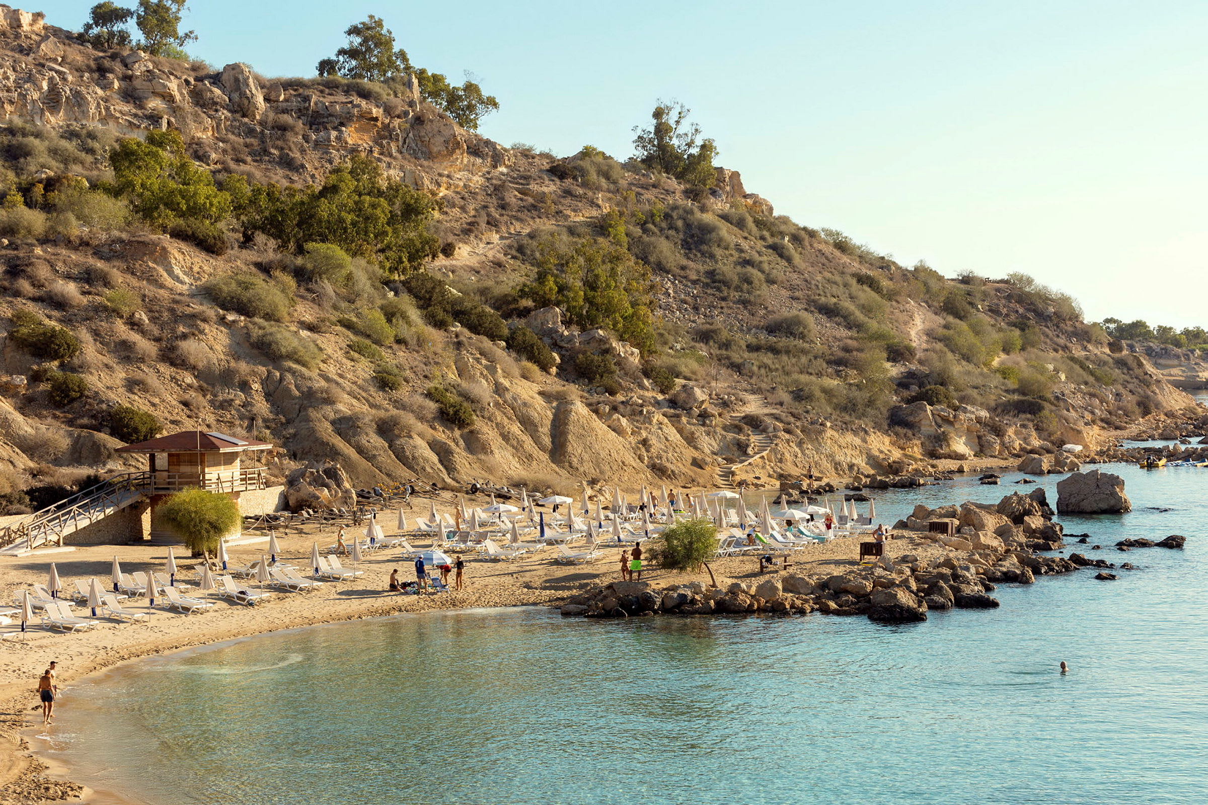 En klippig kust med solstolar och parasoller på en sandstrand. (AI-genererad text)