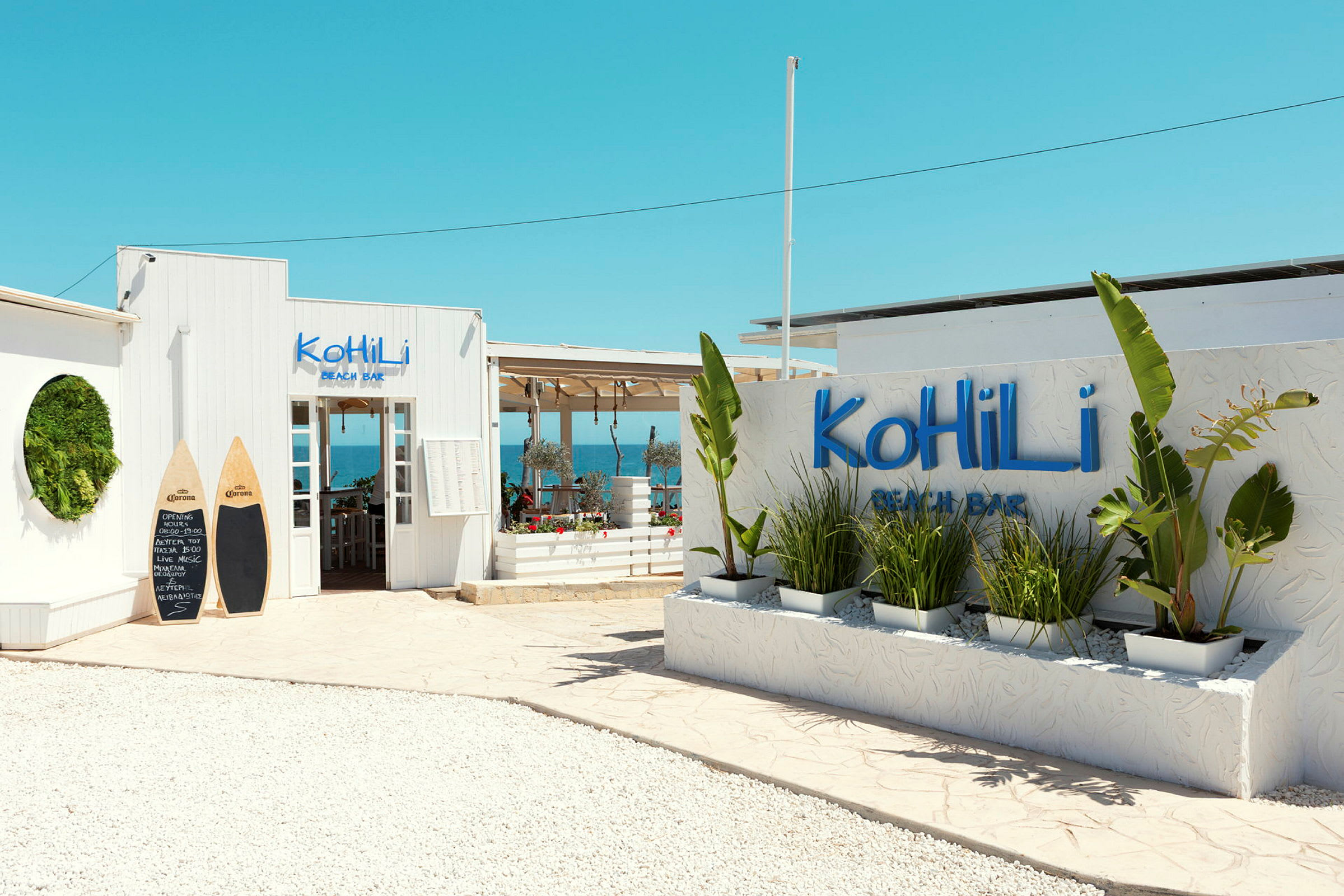 Entré till Kohili Beach Bar med dekorativa växter och en klarblå himmel. (AI-genererad text)