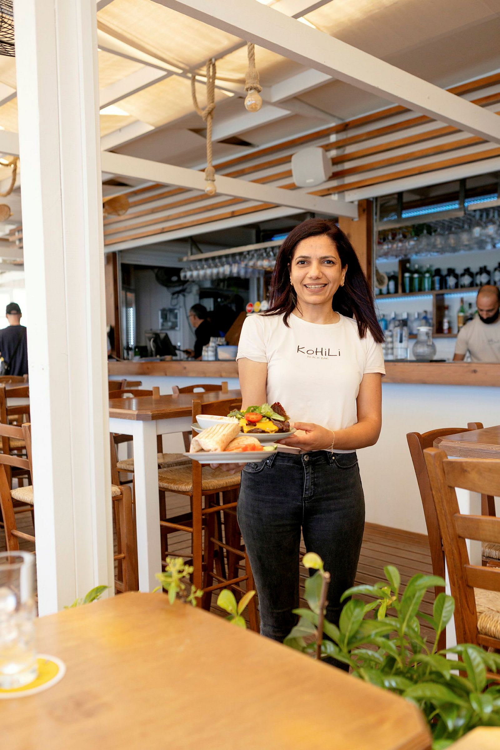 En person håller en tallrik med mat i en restaurang med träinredning och växter i förgrunden. (AI-genererad text)
