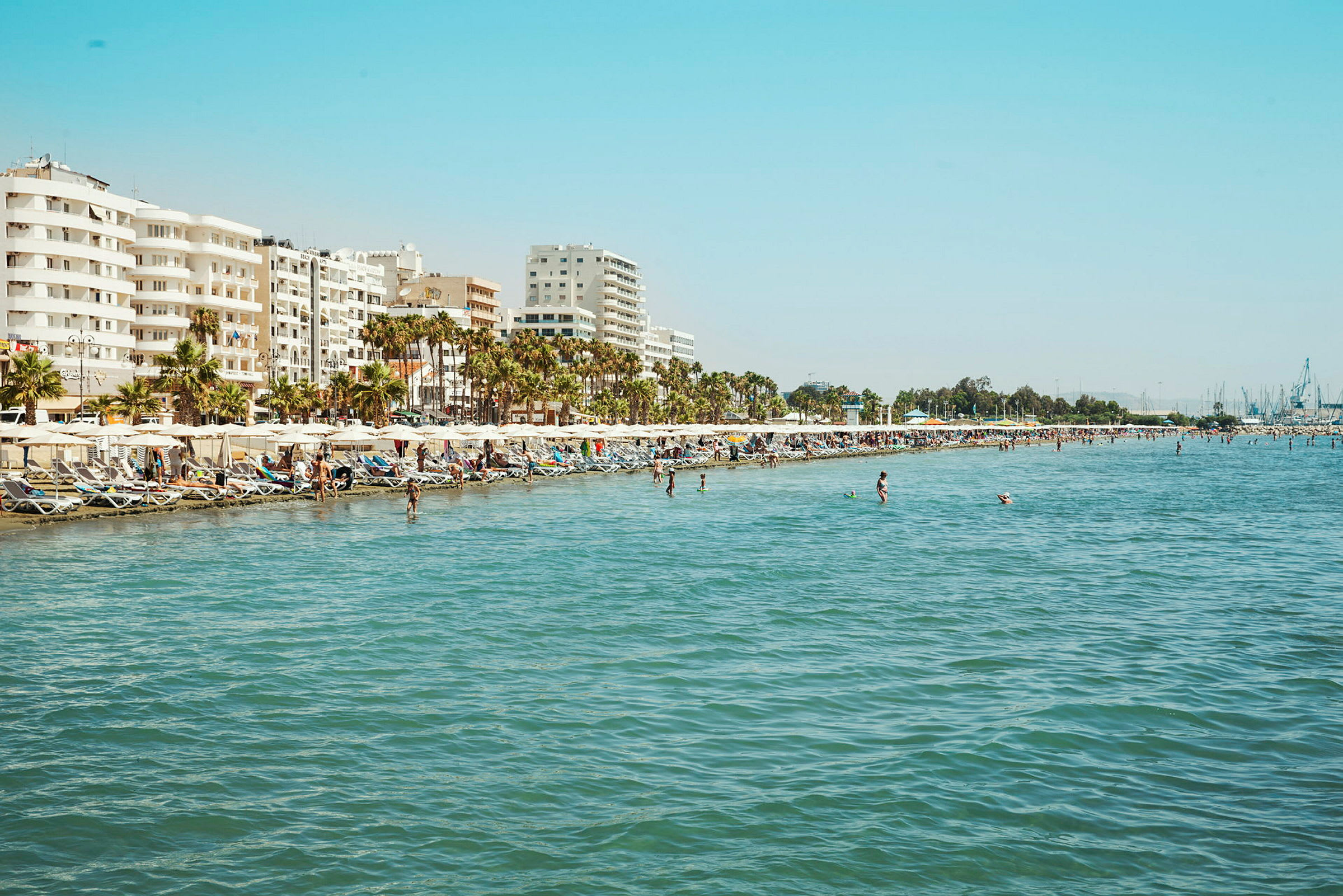 Strand med solstolar och parasoller, vid en stad med flervåningshus. (AI-genererad text)