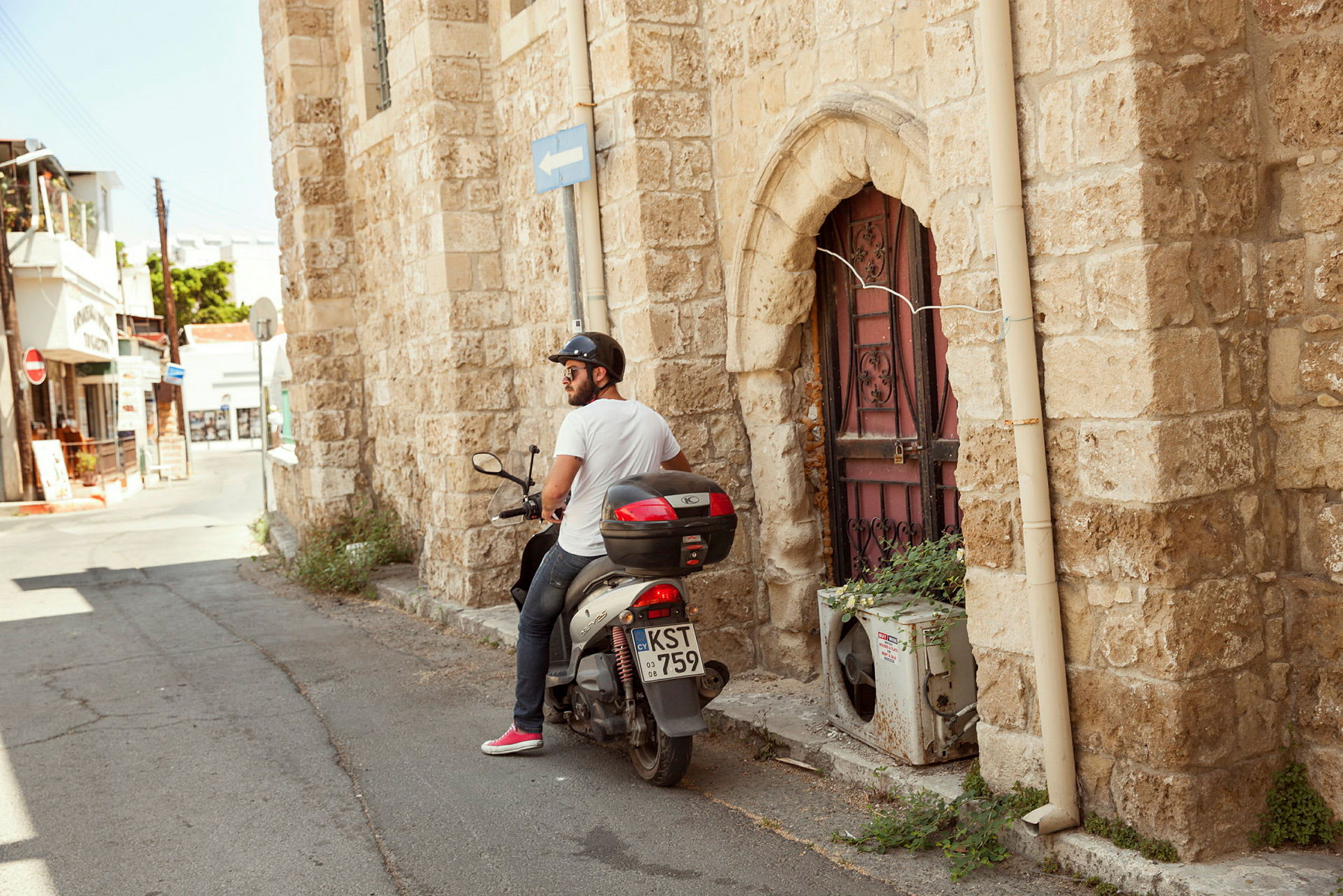 En man sitter på en moped vid en stenbyggnad med en dekorerad dörr. (AI-genererad text)