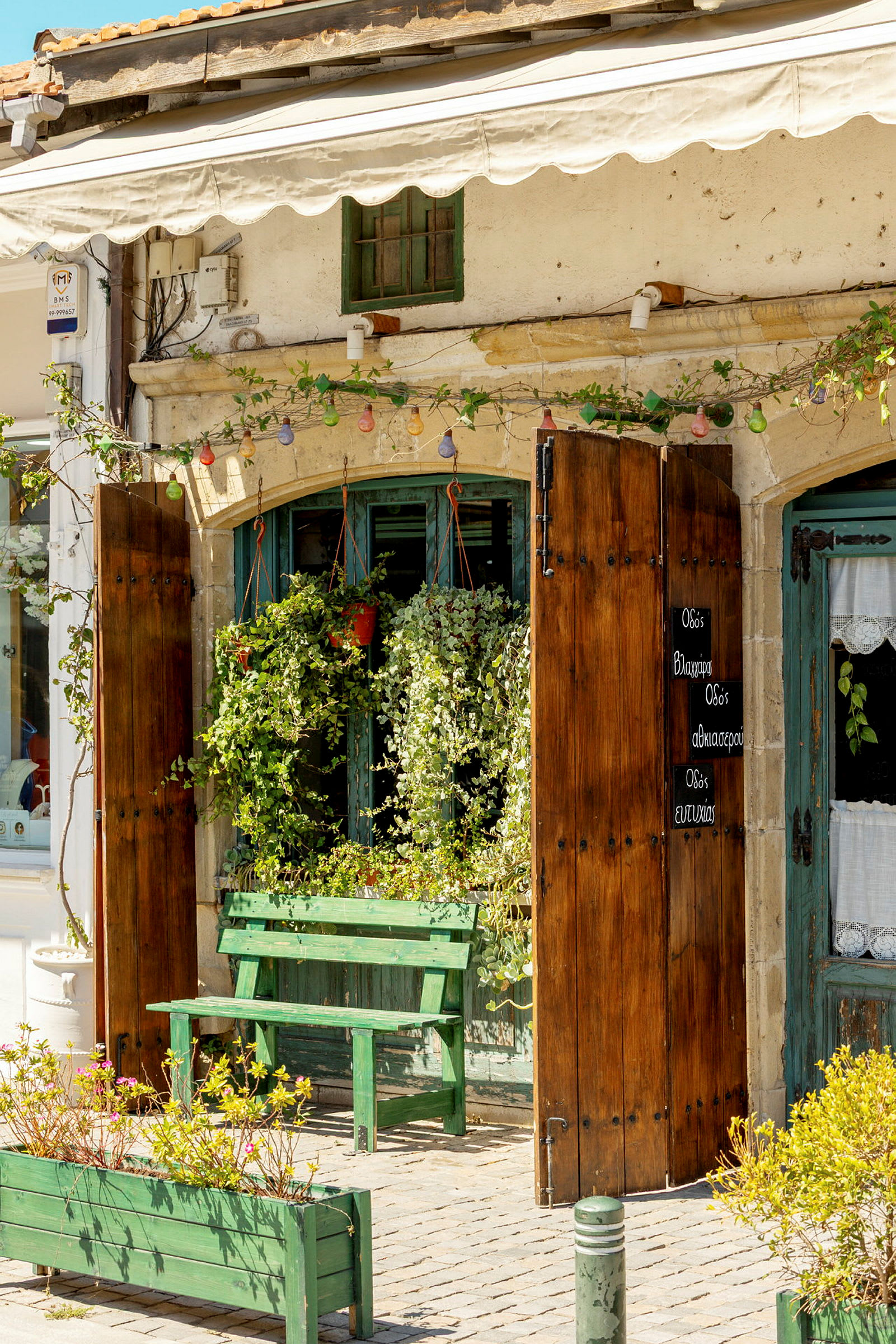 Ett café med träportar, gröna växter och en grön bänk utanför. (AI-genererad text)