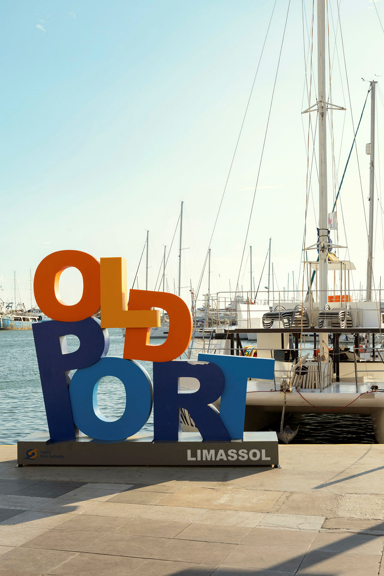 Färgglad skylt med texten 'Old Port' vid hamnen i Limassol, segelbåtar i bakgrunden. (AI-genererad text)