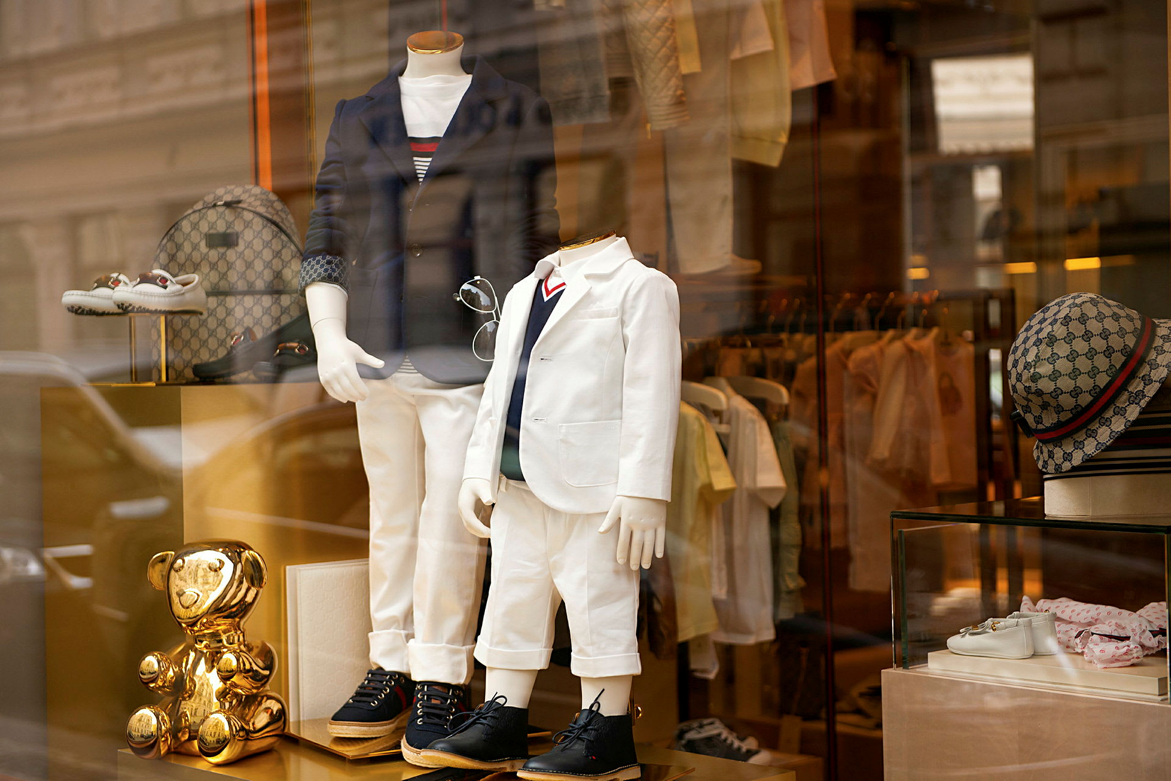 Butiksfönster med två mannequin-dockor klädda i eleganta outfits, omgivna av accessoarer och ett guldigt prydnadsföremål. (AI-genererad text)
