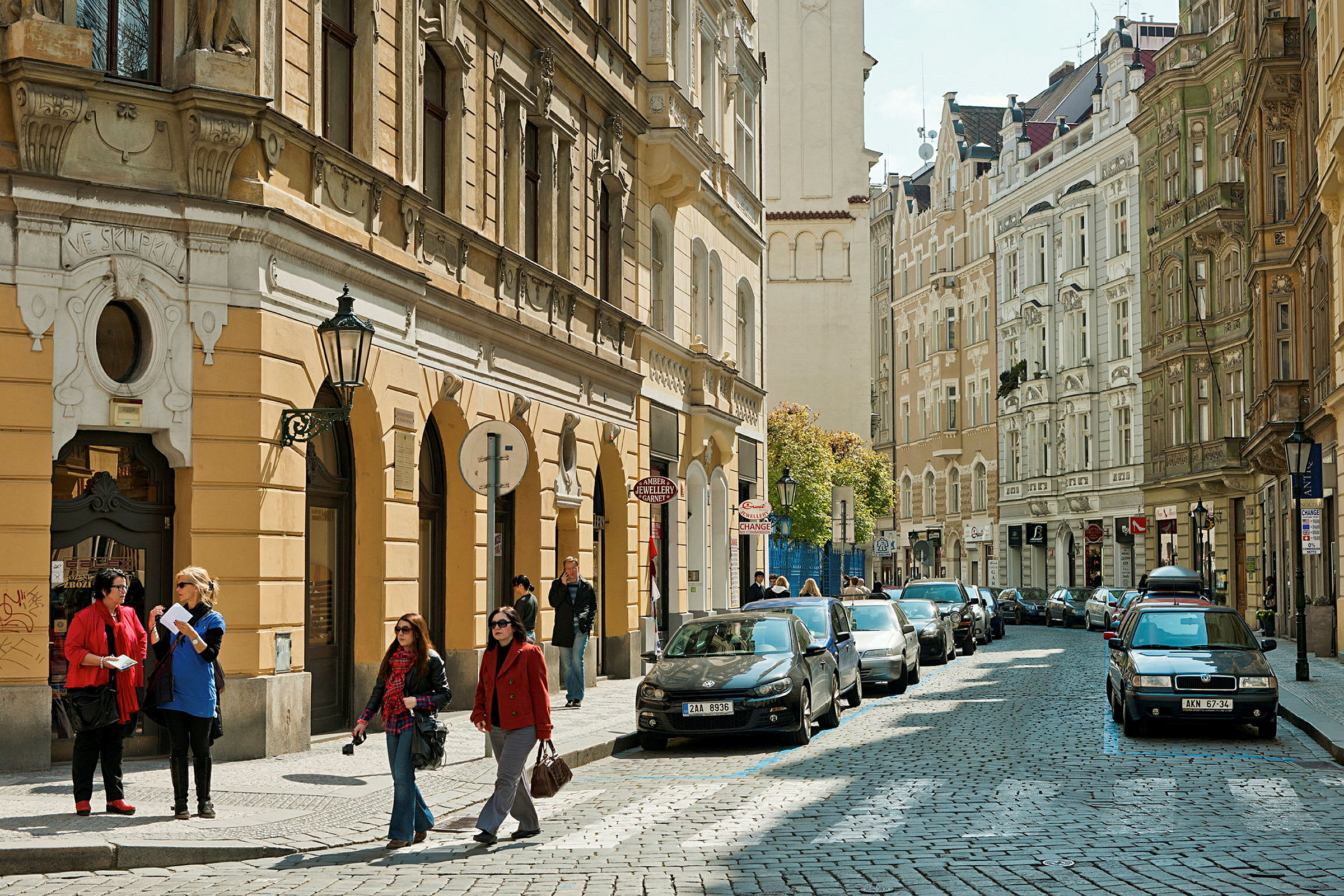 En stadsgata med bilar parkerade längs trottoaren och människor som promenerar. (AI-genererad text)
