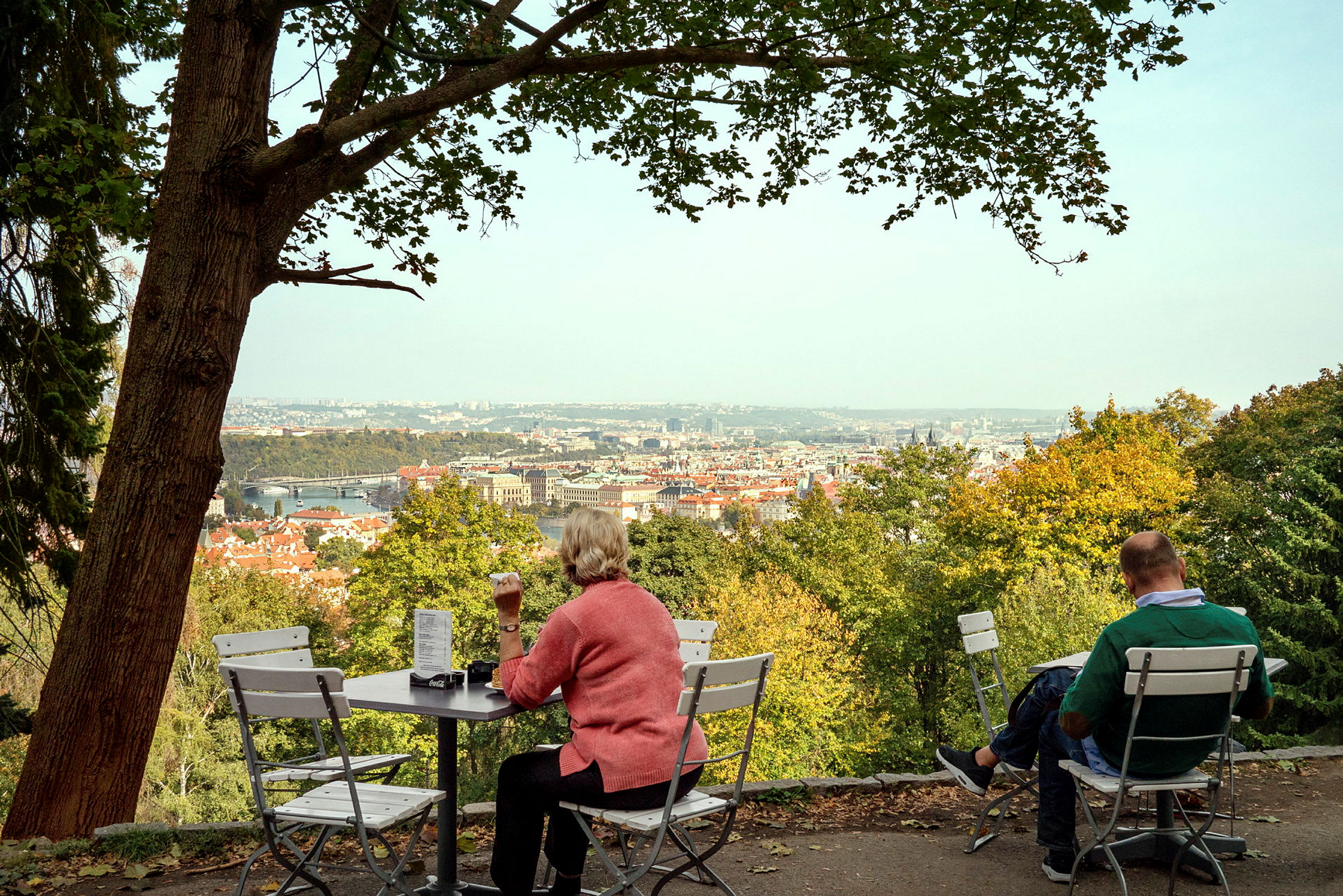 En uteservering med utsikt över en stad omgiven av träd. (AI-genererad text)