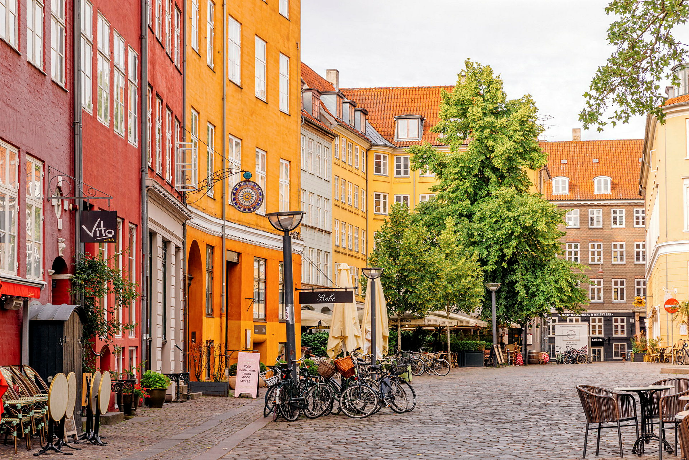 En pittoresk kullerstensgata med färgglada byggnader, cyklar och uteservering under parasoller. (AI-genererad text)