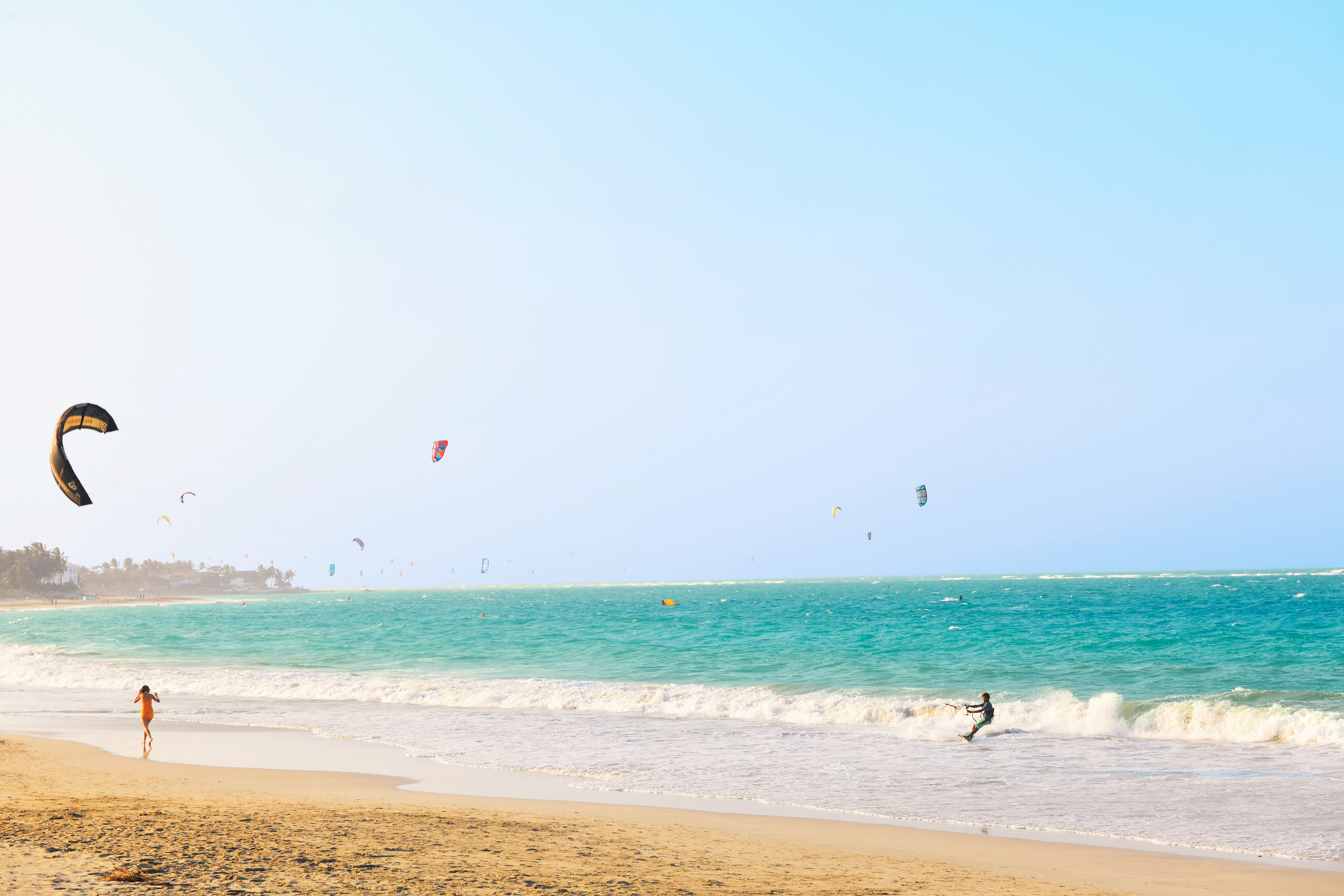En strand med turkost hav och många kitesurfare. (AI-genererad text)