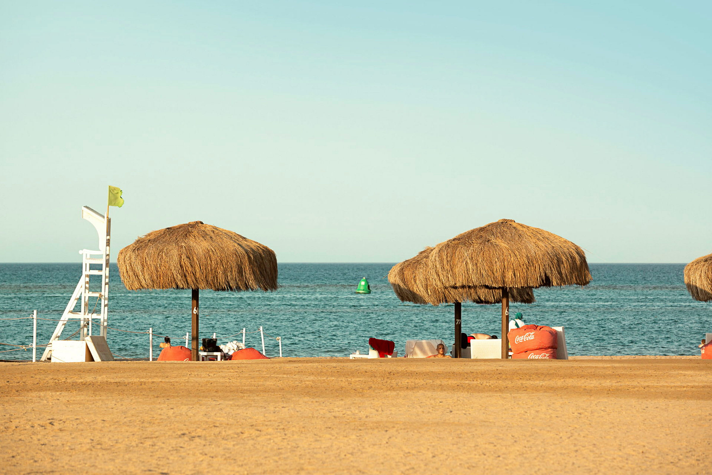 Strand med halmtakparaplyer och hav i bakgrunden. (AI-genererad text)