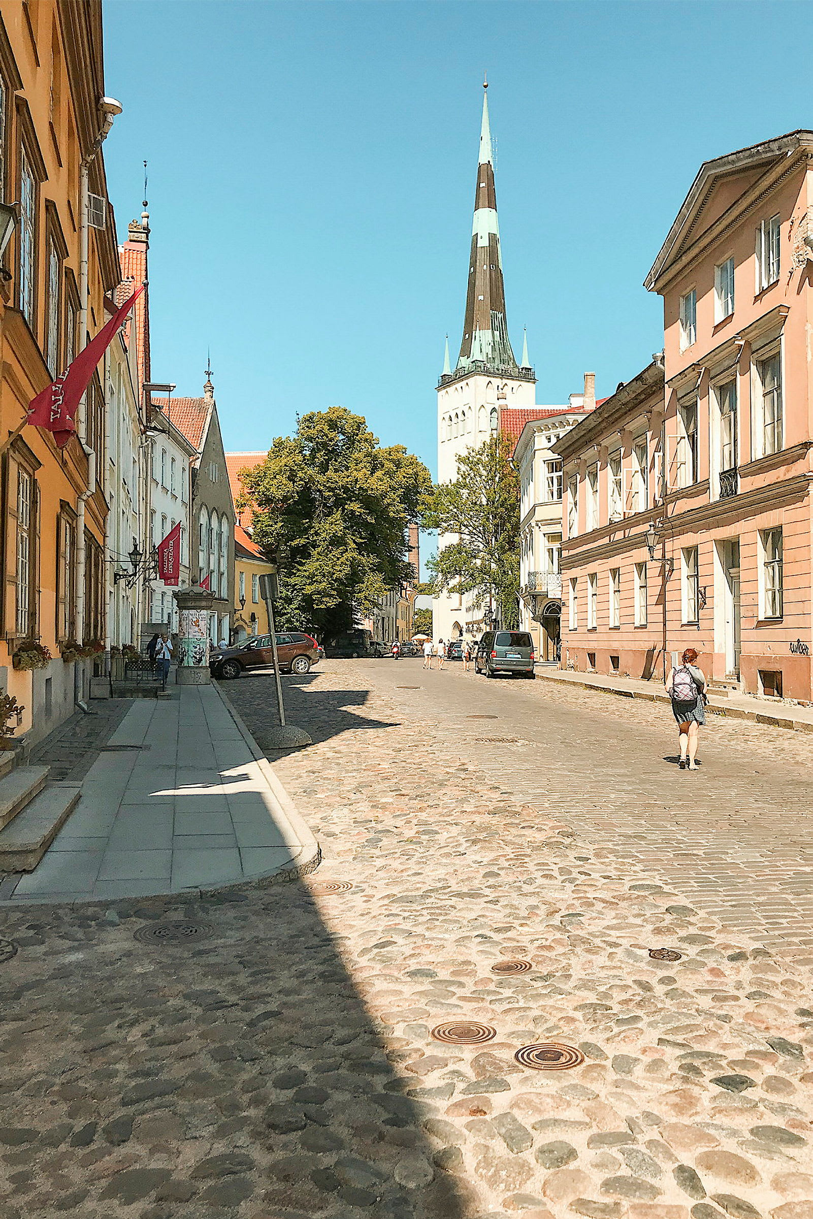 En stenbelagd gata kantad med färgglada äldre byggnader, med en kyrkospira synlig i bakgrunden under en klar blå himmel. (AI-genererad text)