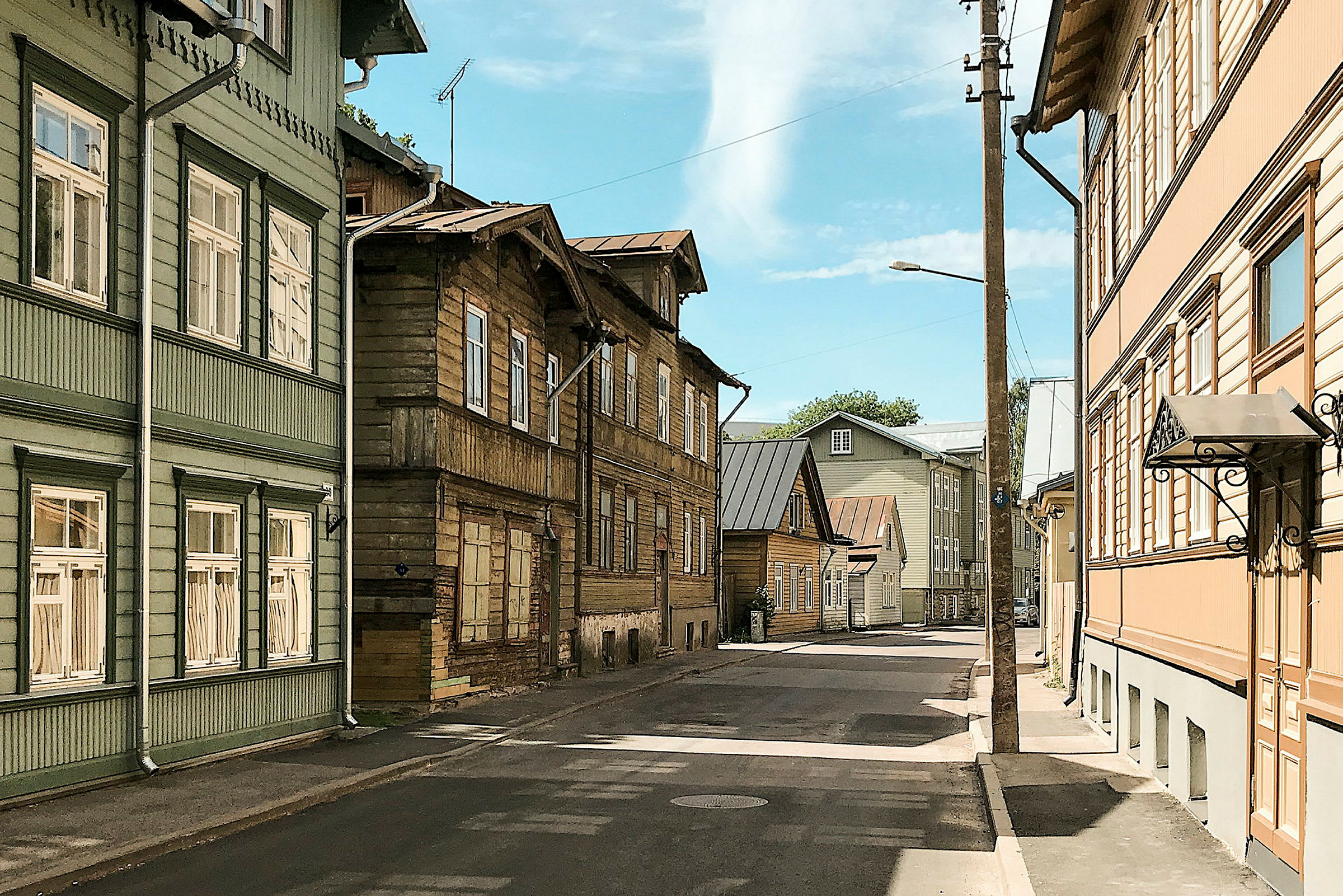 En gata kantad av hus i trä med olika färger, blå himmel syns i bakgrunden. (AI-genererad text)