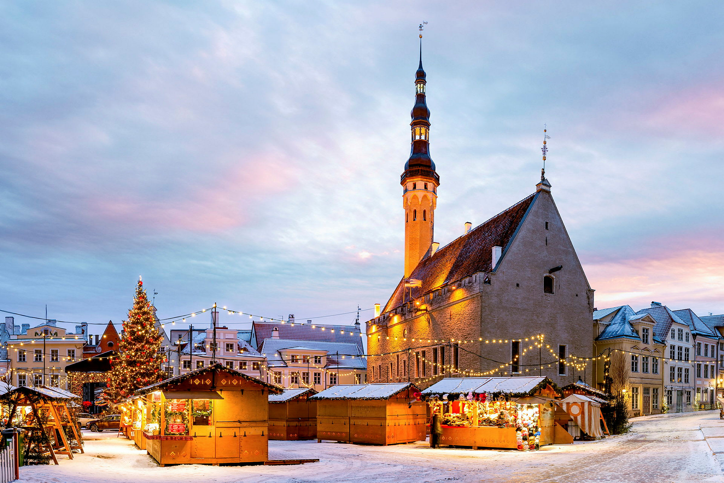 En julmarknad med träbodar, en stor julgran och en historisk byggnad i bakgrunden. (AI-genererad text)