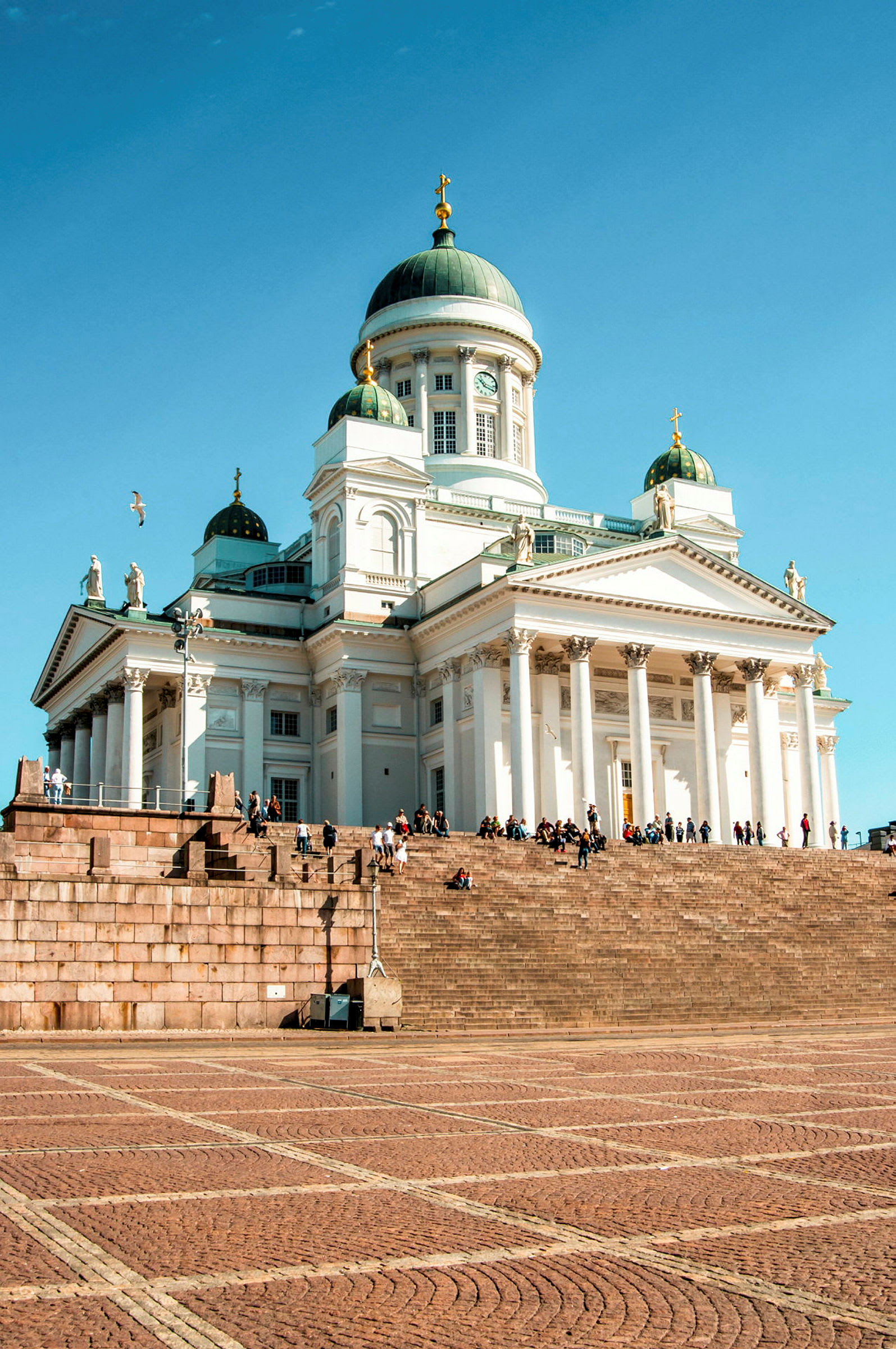 Stora trappsteg leder upp till en vit domkyrka med gröna kupoler. (AI-genererad text)