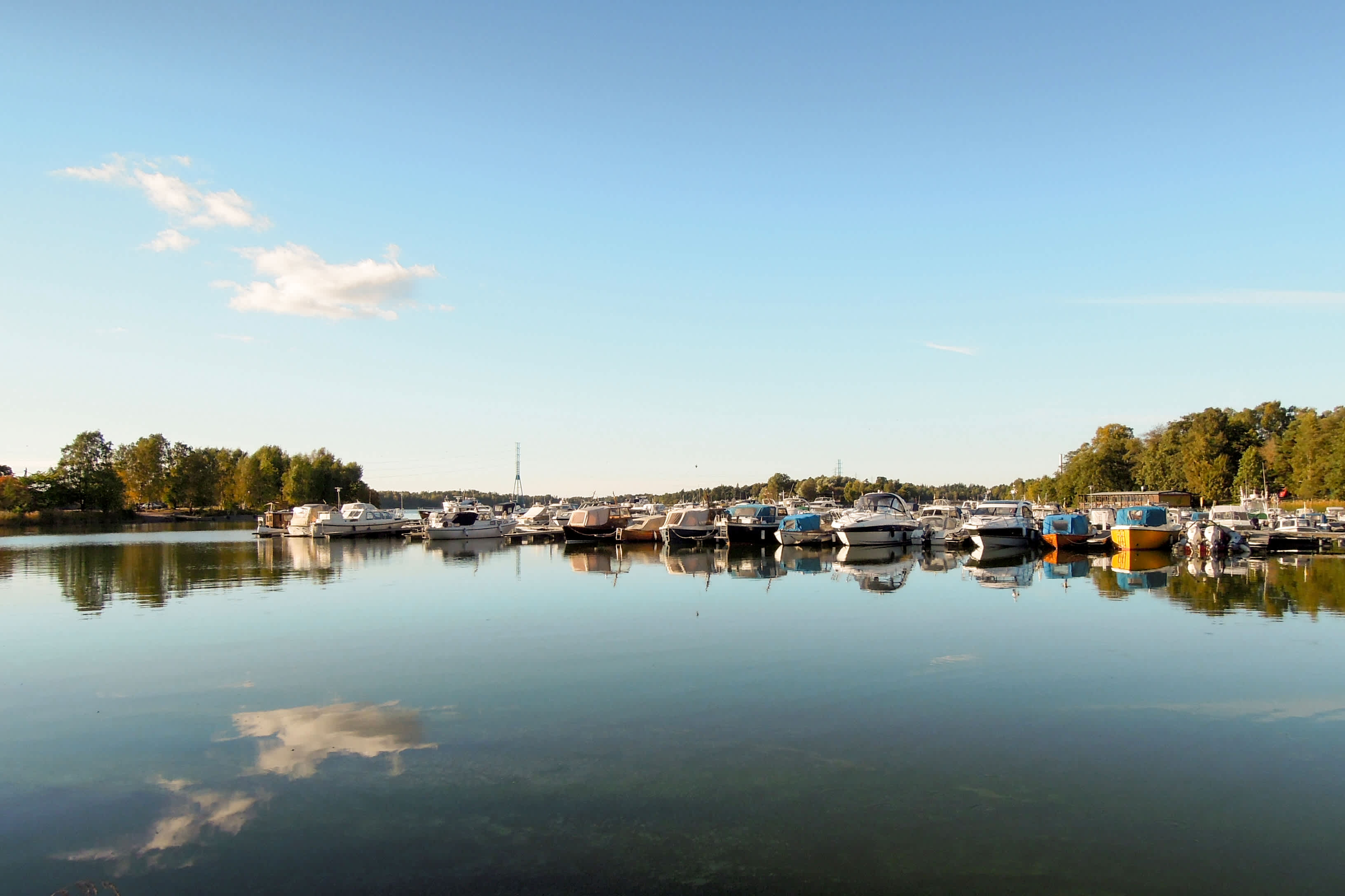 En småbåtshamn vid en stilla vattenyta med båtar och omgivande träd. (AI-genererad text)