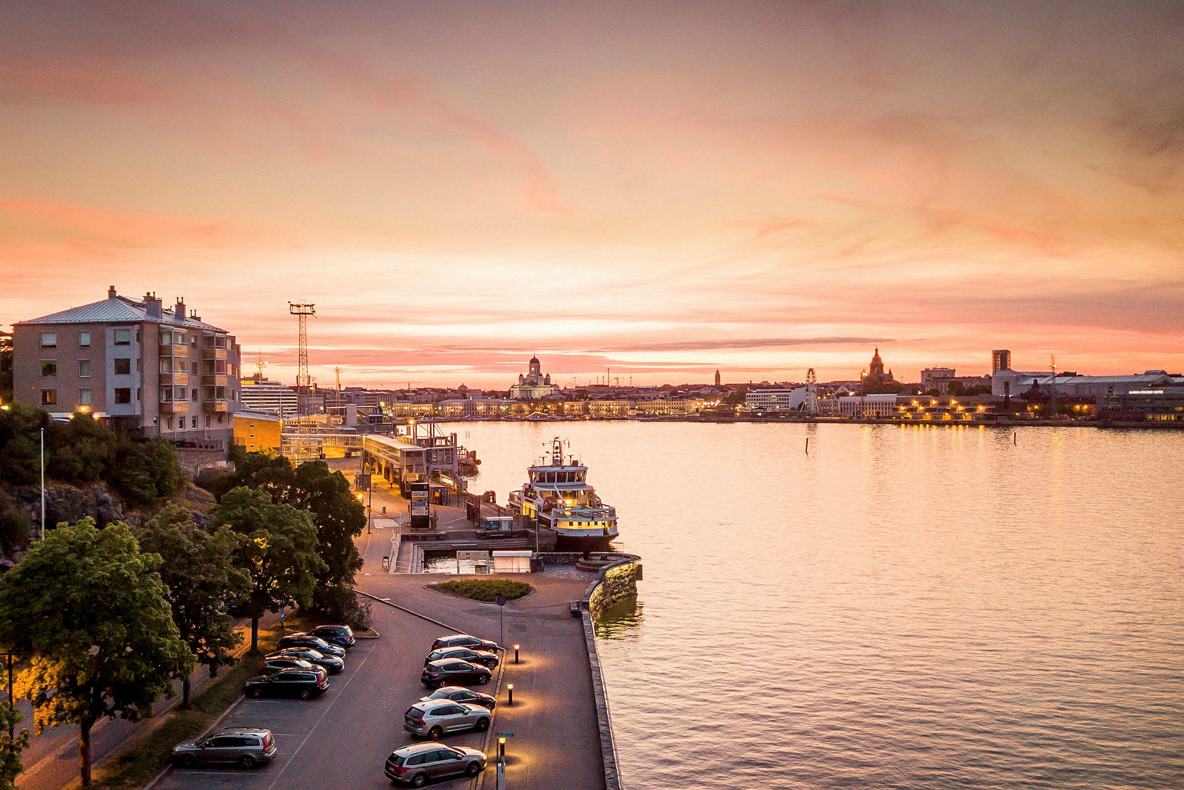 En stadsutsikt över en kust med kvällsbelysning och en färja vid kajen. (AI-genererad text)