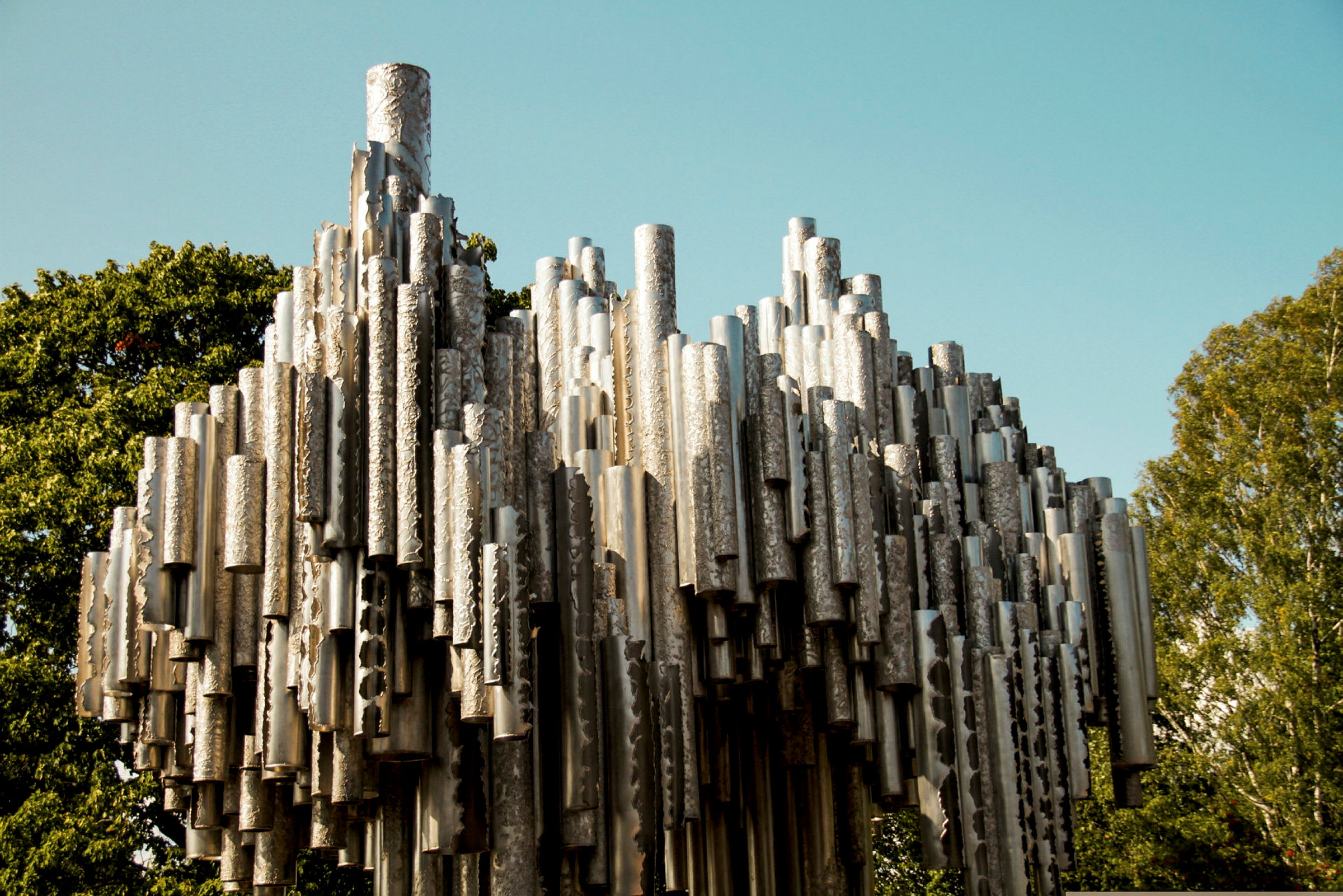 En metallskulptur omgiven av gröna träd med klar blå himmel i bakgrunden. (AI-genererad text)