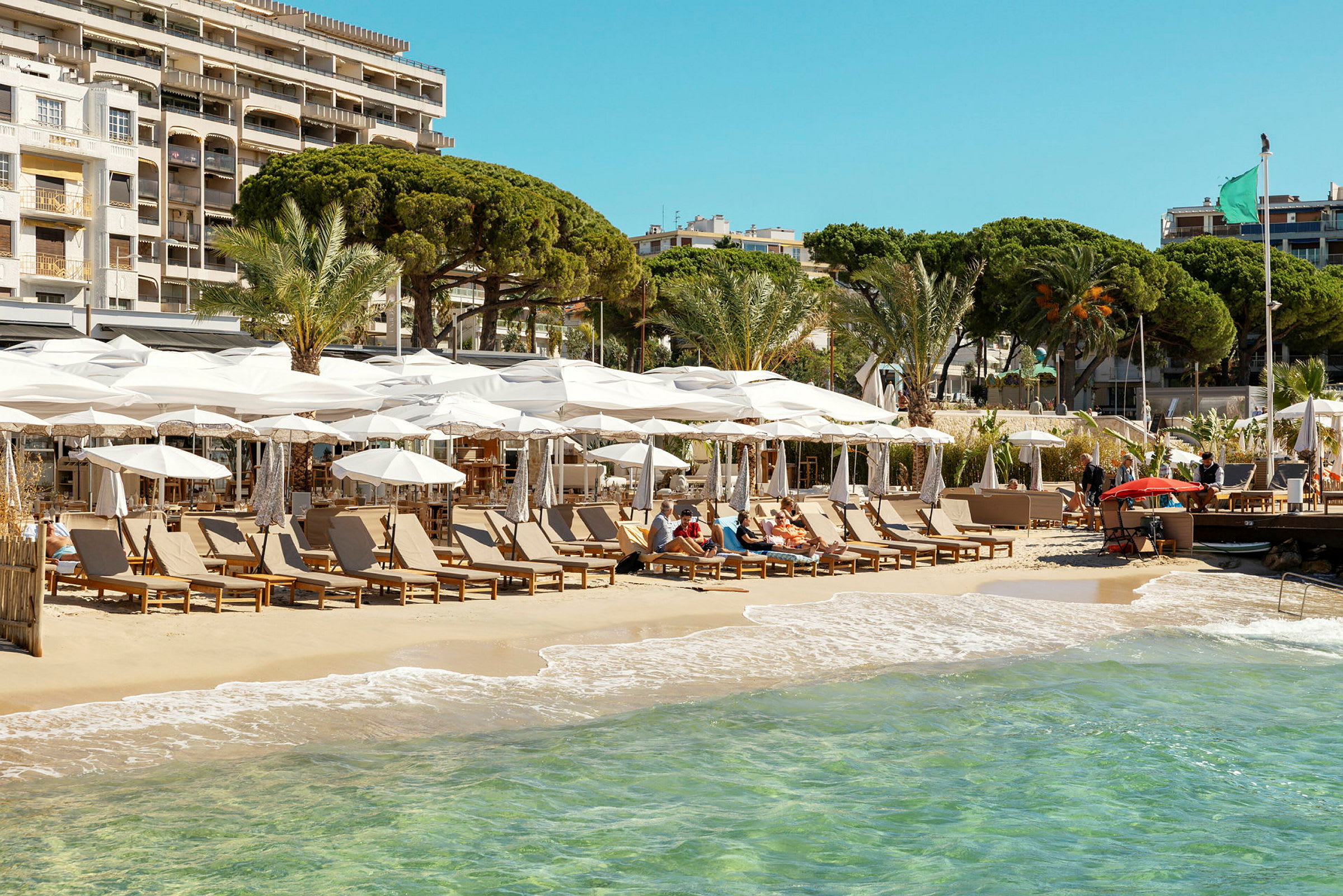 Strand med solstolar och parasoller vid kanten av kristallklart vatten. (AI-genererad text)