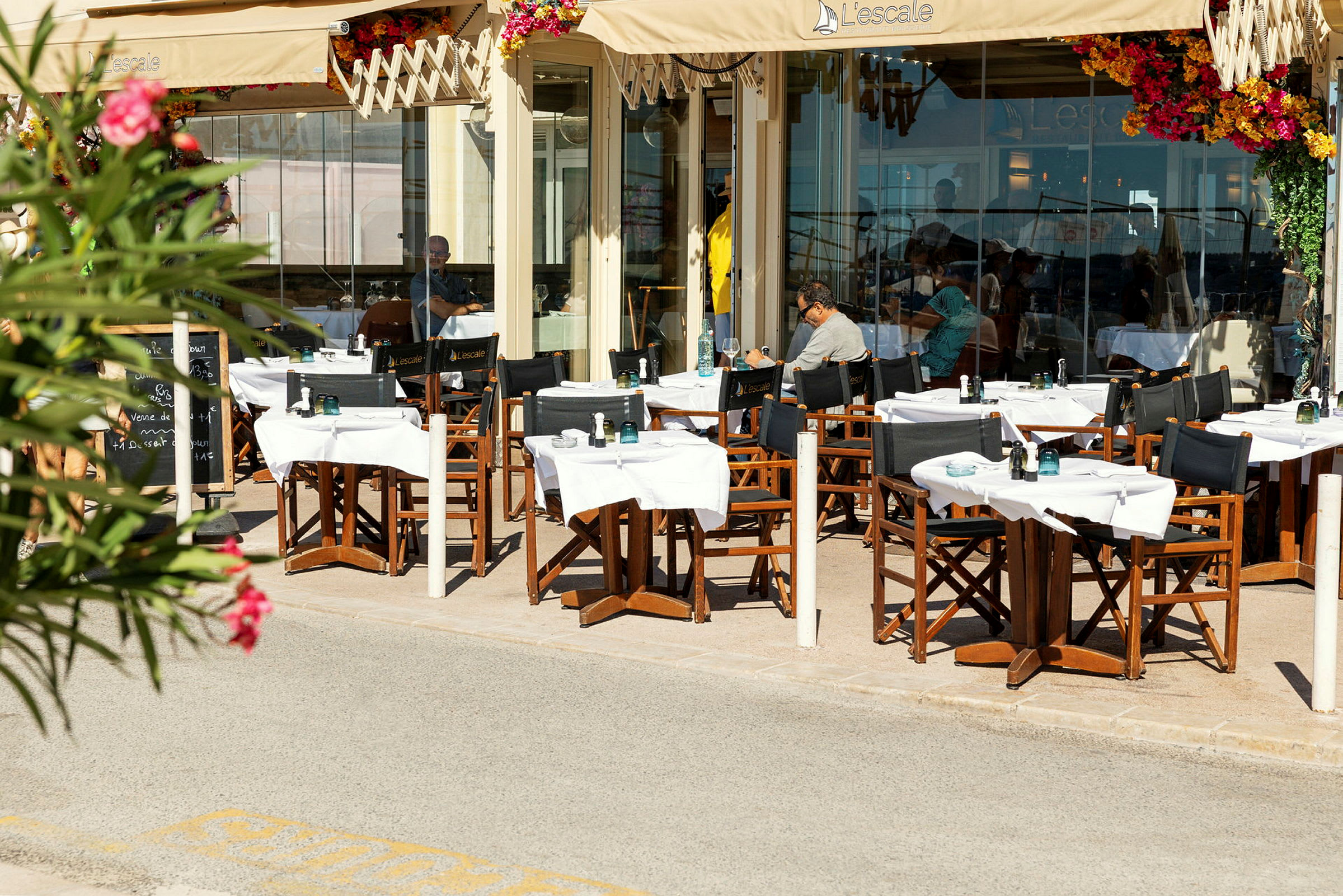 Uteservering vid en restaurang med bord och stolar under ett soltak. (AI-genererad text)