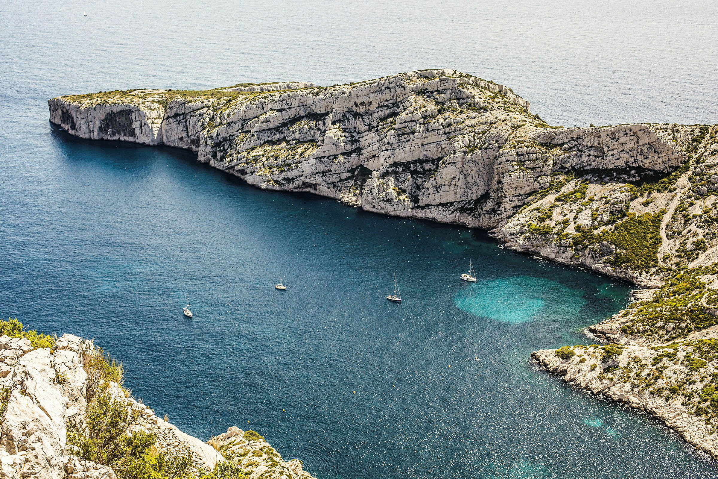 En vik med klart vatten och segelbåtar, omgiven av klippor. (AI-genererad text)