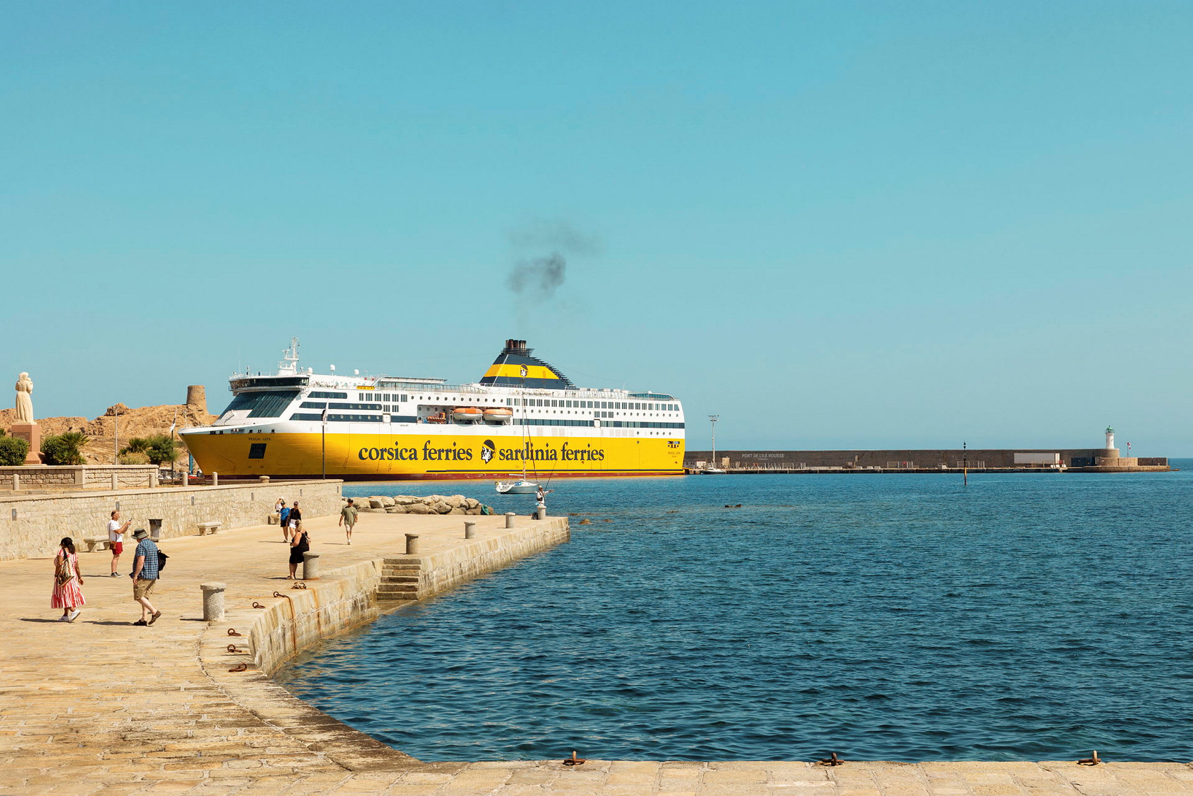 En gul och vit färja från Corsica Ferries ligger vid kajen, med människor som promenerar på kajområdet och havet synligt i förgrunden. (AI-genererad text)
