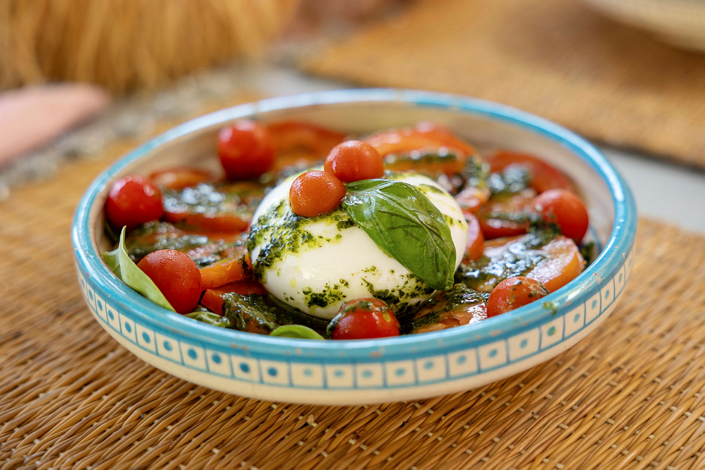 En tallrik med burrata, körsbärstomater, färsk basilika och pesto. (AI-genererad text)
