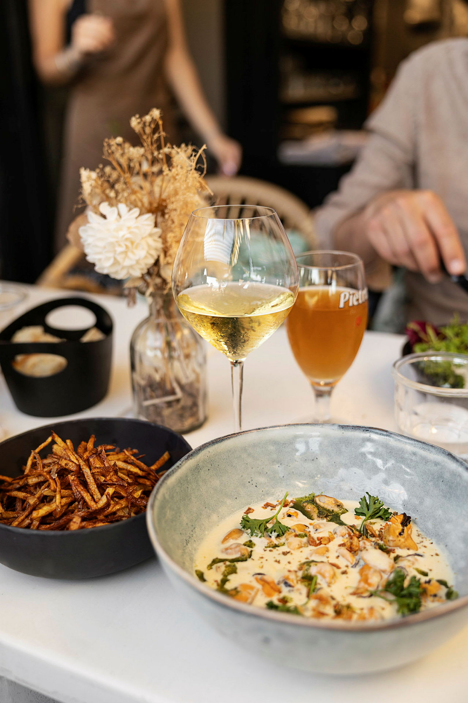 En tallrik med mat, ett glas vitt vin och en skål med pommes frites på ett bord. (AI-genererad text)